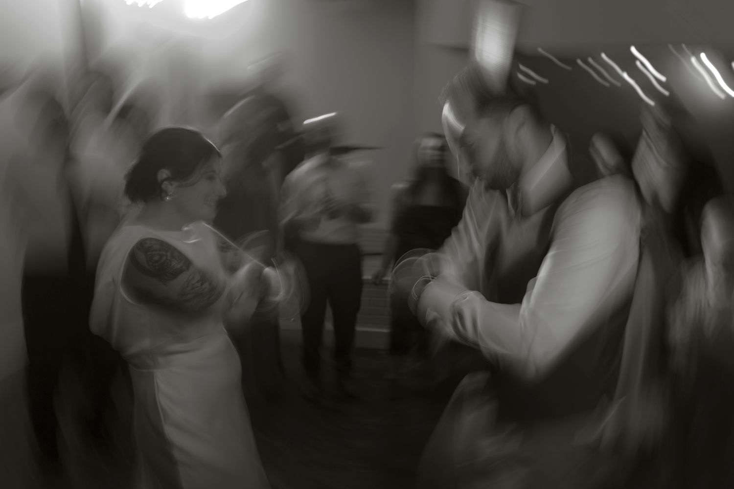 Motion-blurred black and white photo of people dancing at a wedding reception.