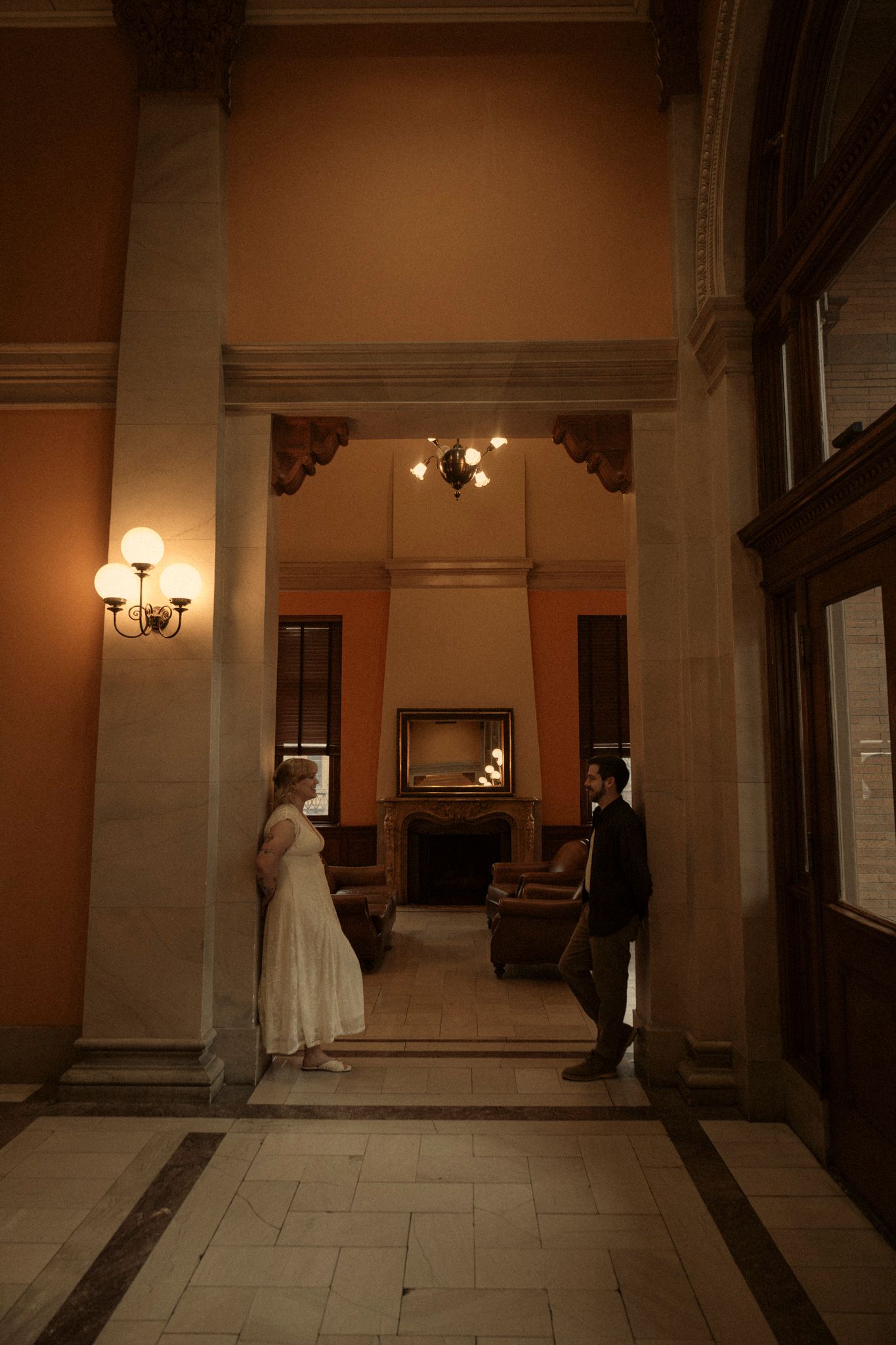 A dimly lit hallway in a historic building with ornate wall sconces and classical architectural details.