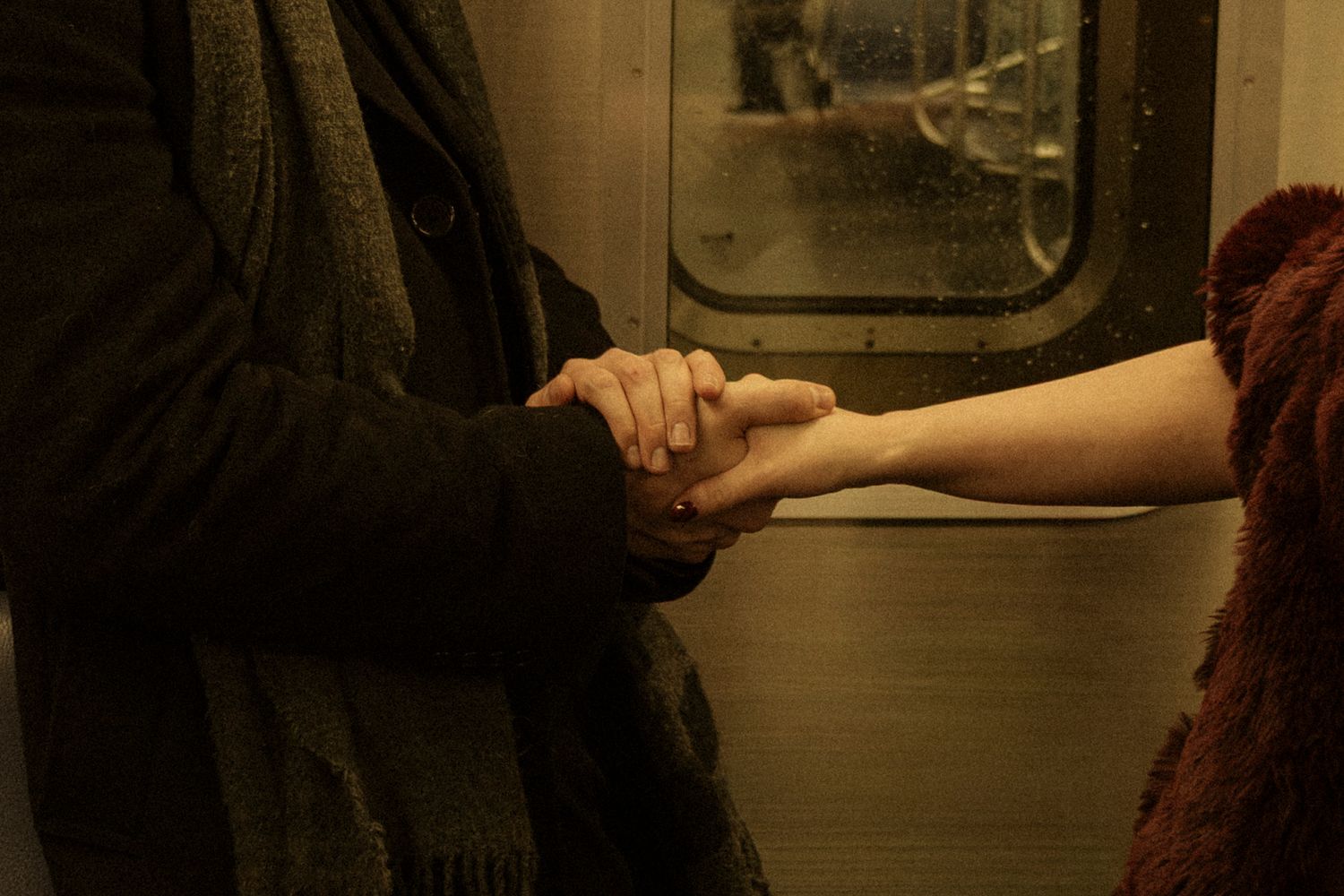 Two hands clasped together in an intimate moment on a subway train.