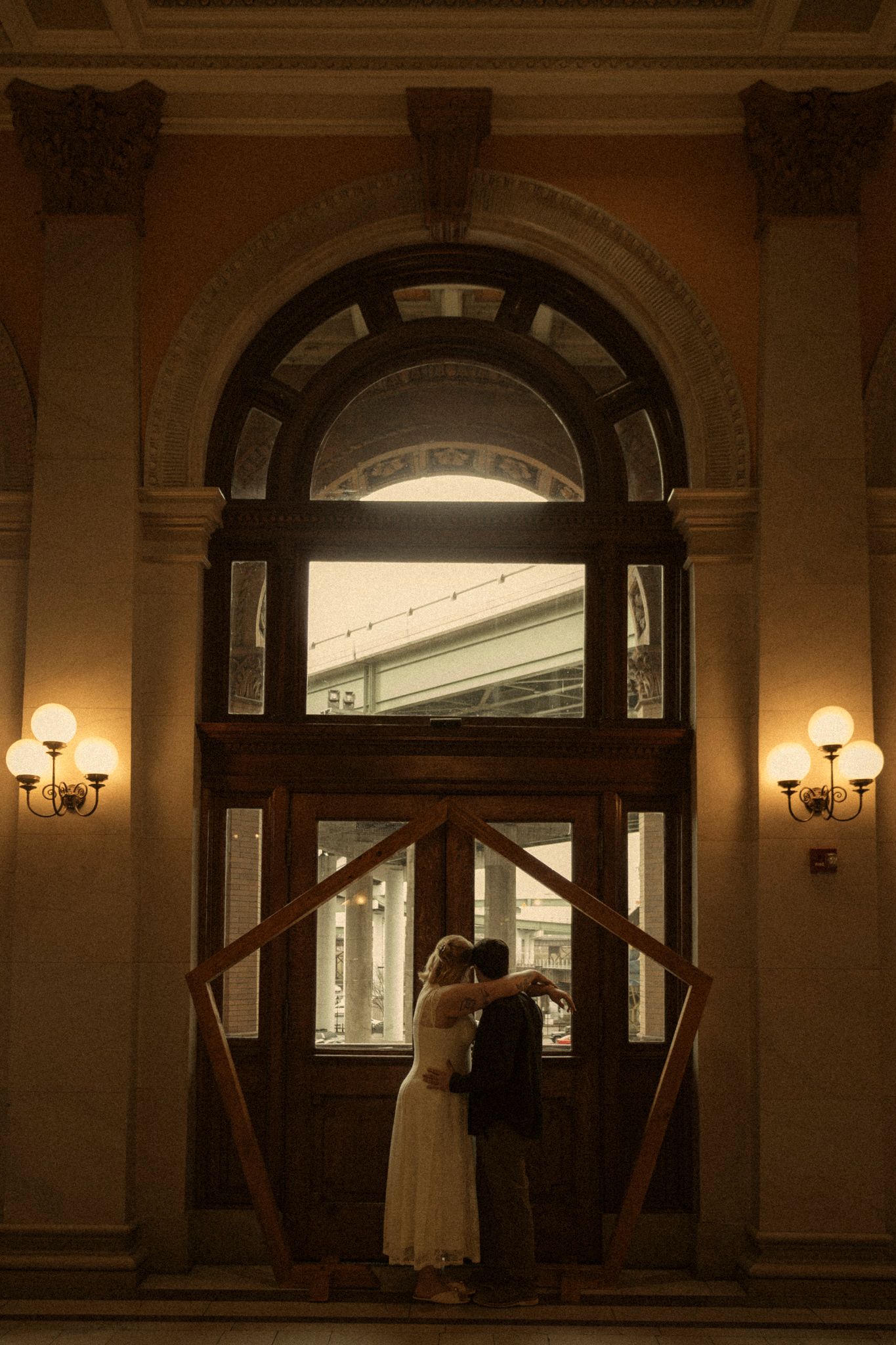 A romantic silhouette stands in an elegant arched doorway with warm lighting in a historic building interior.