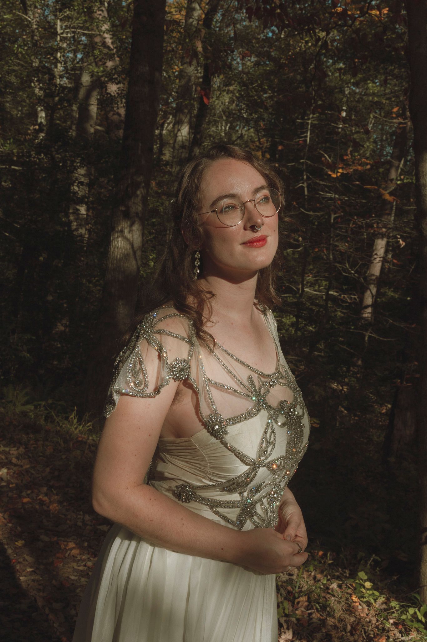 A person in a flowy sage green dress poses thoughtfully in a wooded forest setting during golden hour.