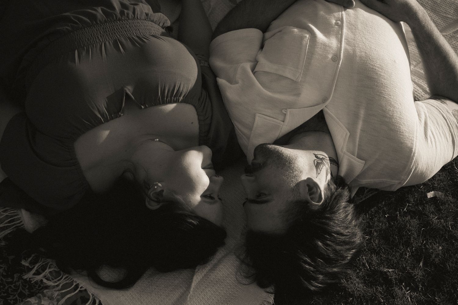 Black and white romantic photo of couple lying on grass facing each other in an intimate moment.