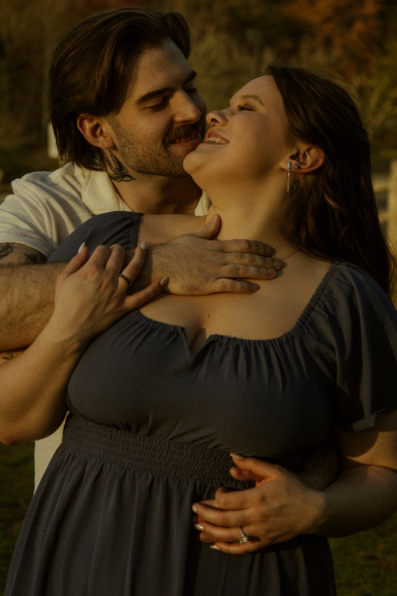 Romantic couple embracing at sunset outdoors, man kissing woman's cheek as she smiles joyfully.
