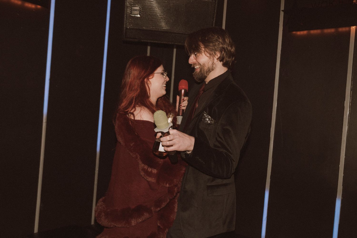 Two people dancing together in a dimly lit room with dark walls and vertical light bars.