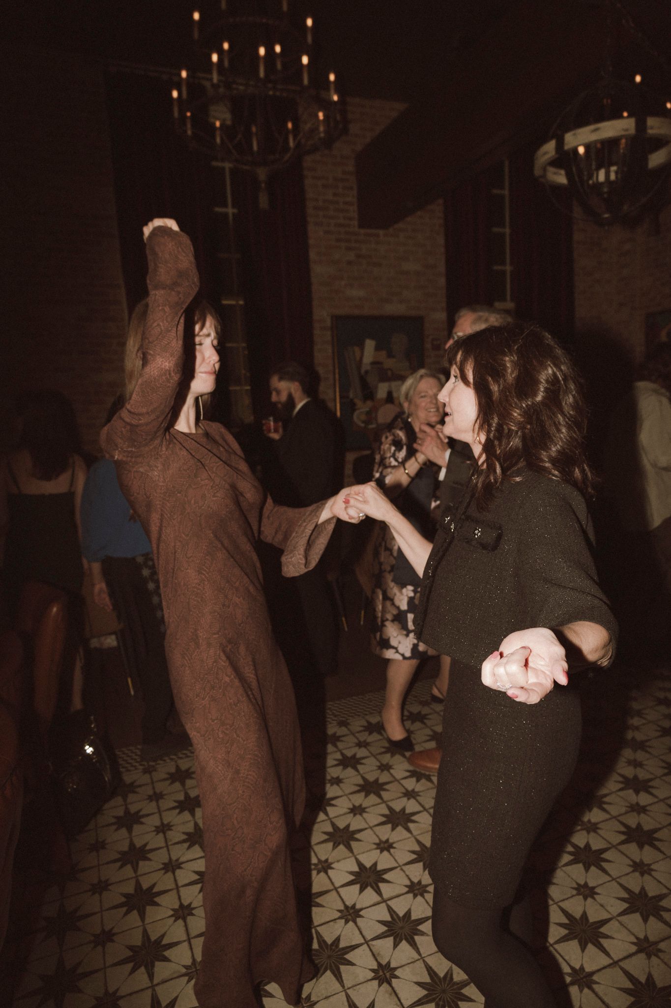 Two women dancing together at a candlelit venue with patterned tile floors during a festive event.