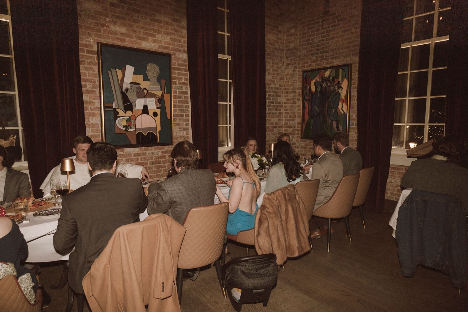 Guests seated at tables during an elegant wedding reception dinner in a brick-walled restaurant with artwork.