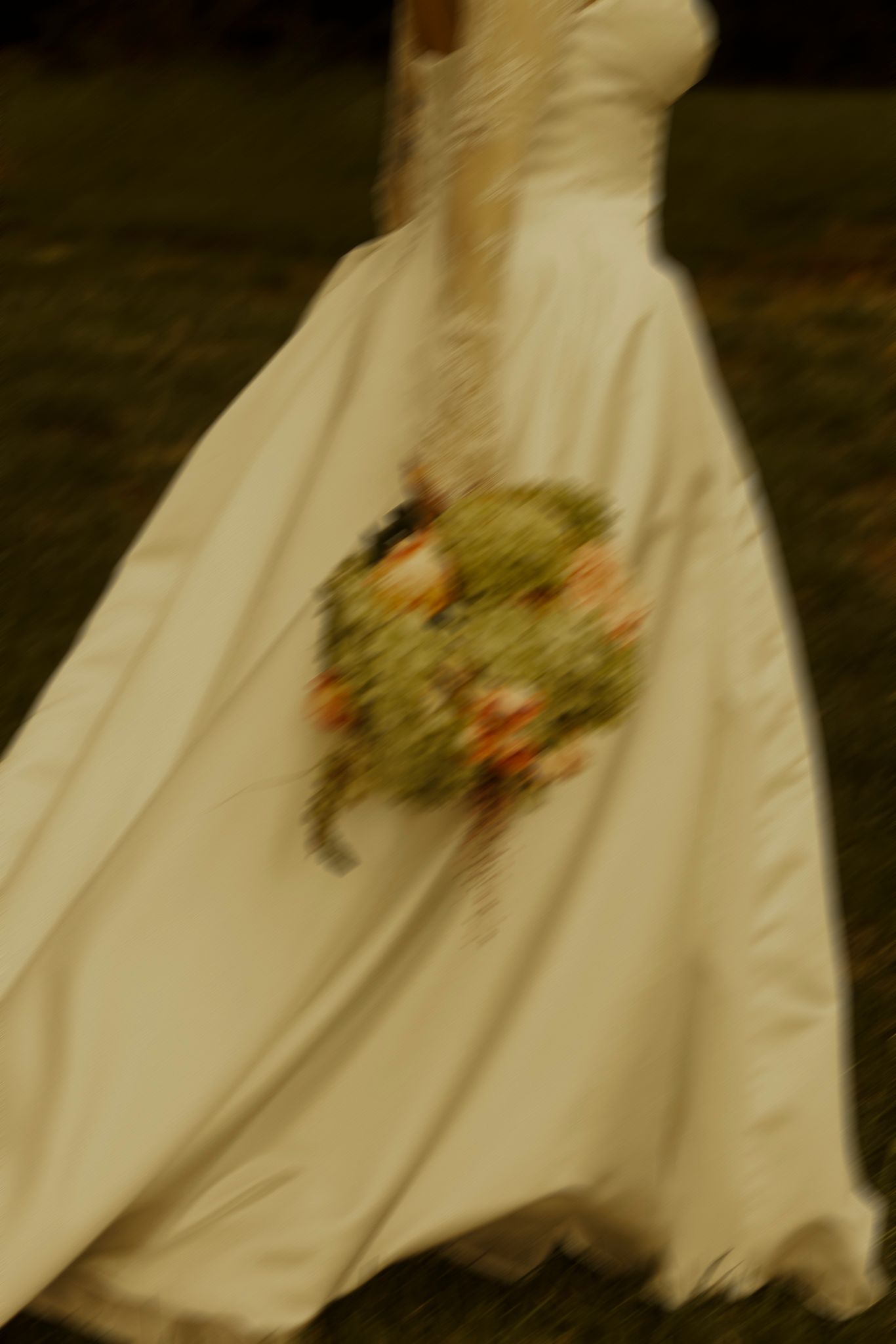 Blurred motion shot of a bride in a white wedding gown holding a colorful floral bouquet while walking outdoors.