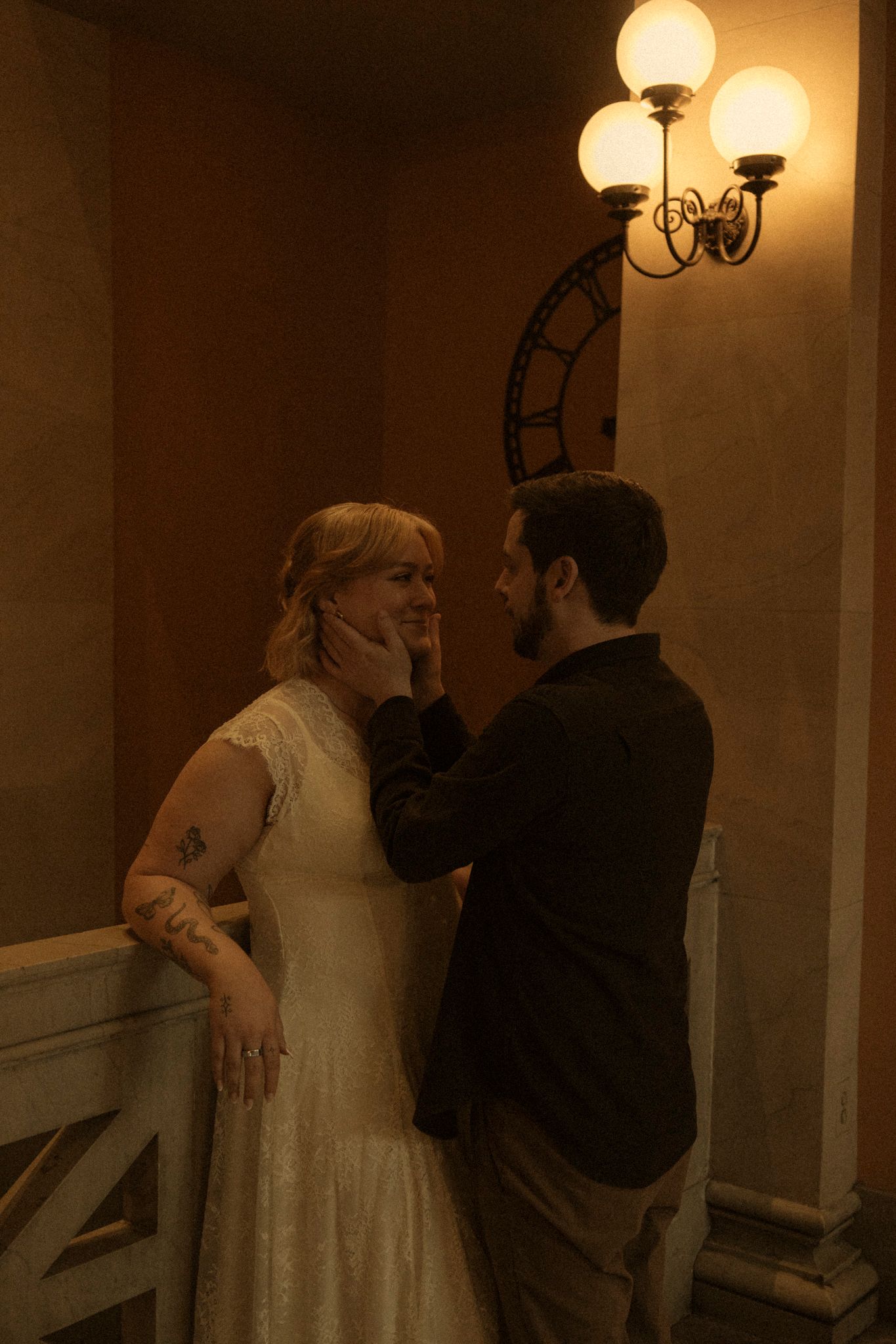 Two figures embrace in a warmly lit hallway with ornate wall sconces casting a romantic glow.