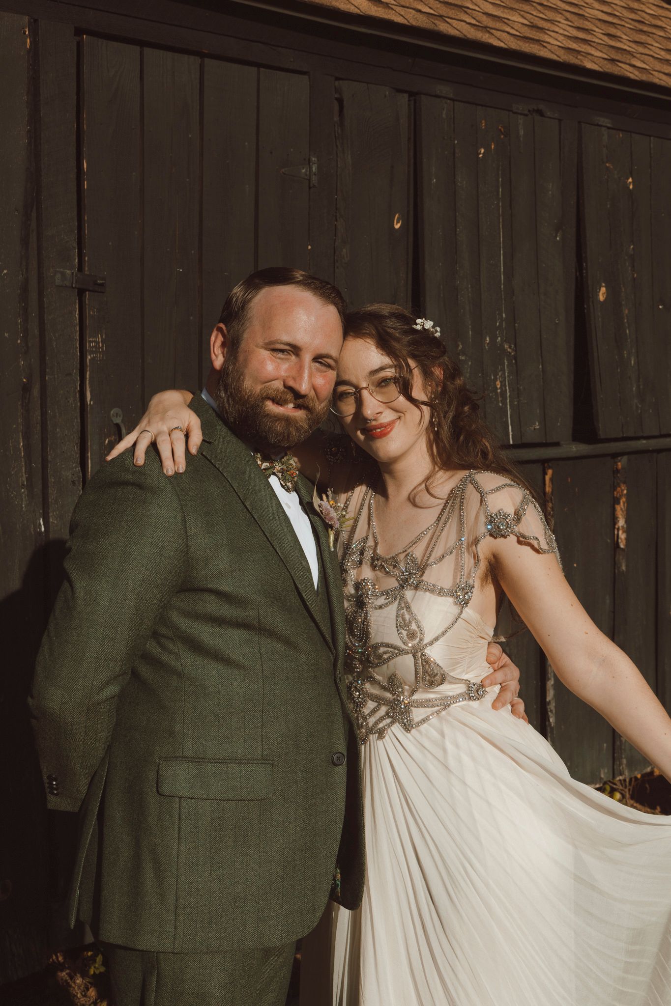 A couple shares a romantic moment in a rustic setting, with the bride wearing white and groom in dark green attire.