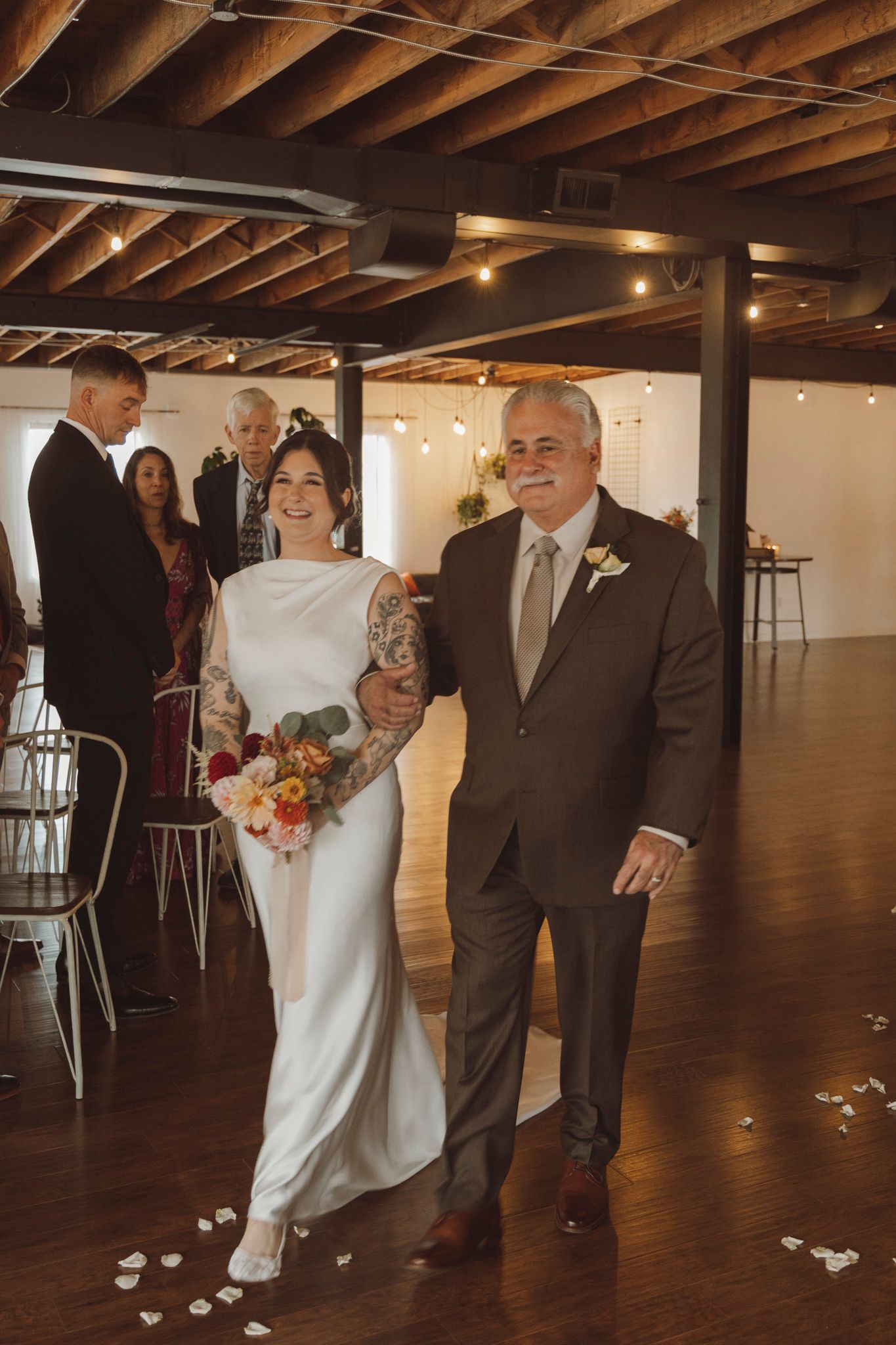 Wedding party walking across a spacious venue with exposed wooden beams and dark hardwood floors.