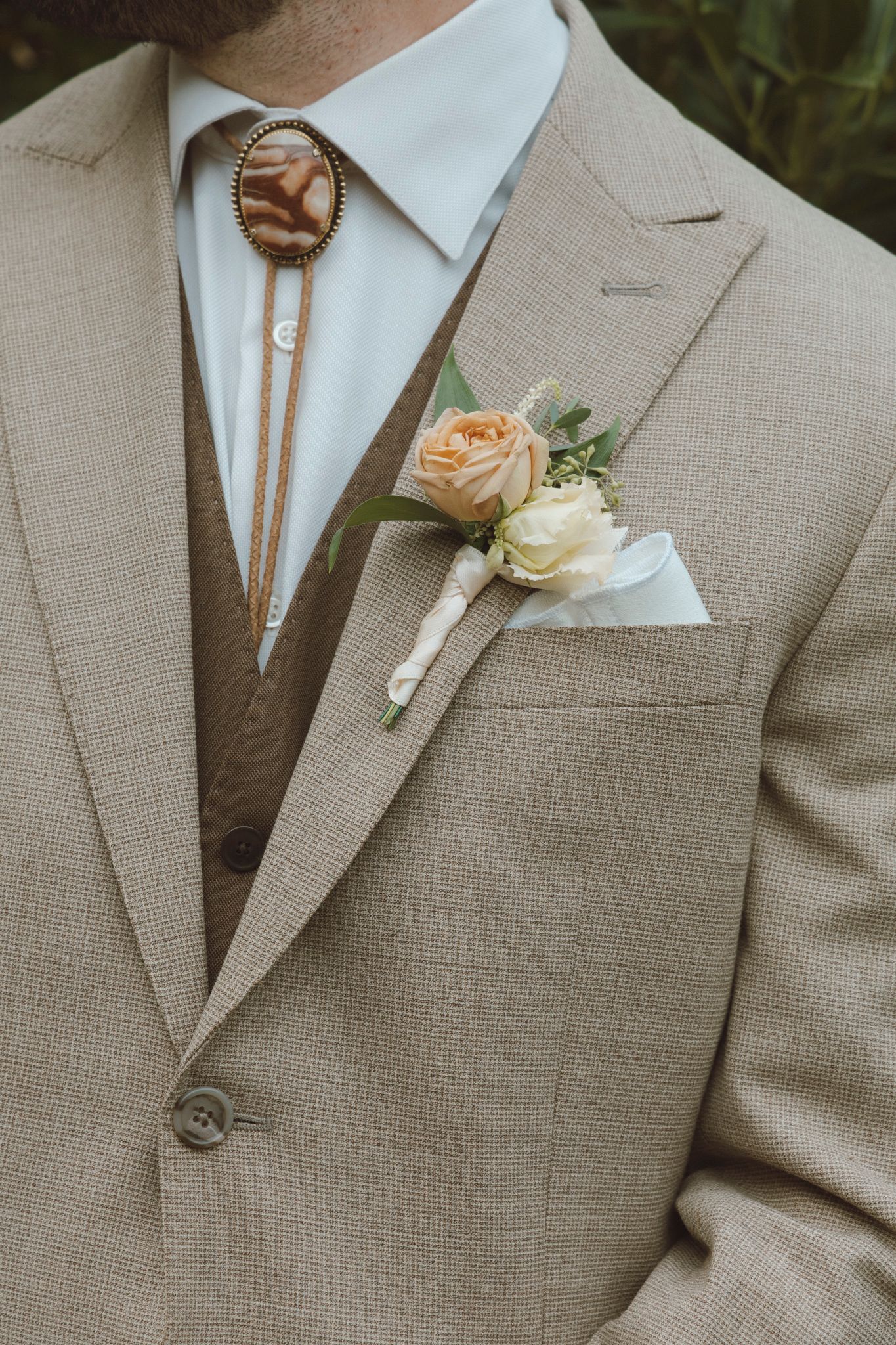 Close-up details of tan suit jackets with floral boutonnieres at a wedding.