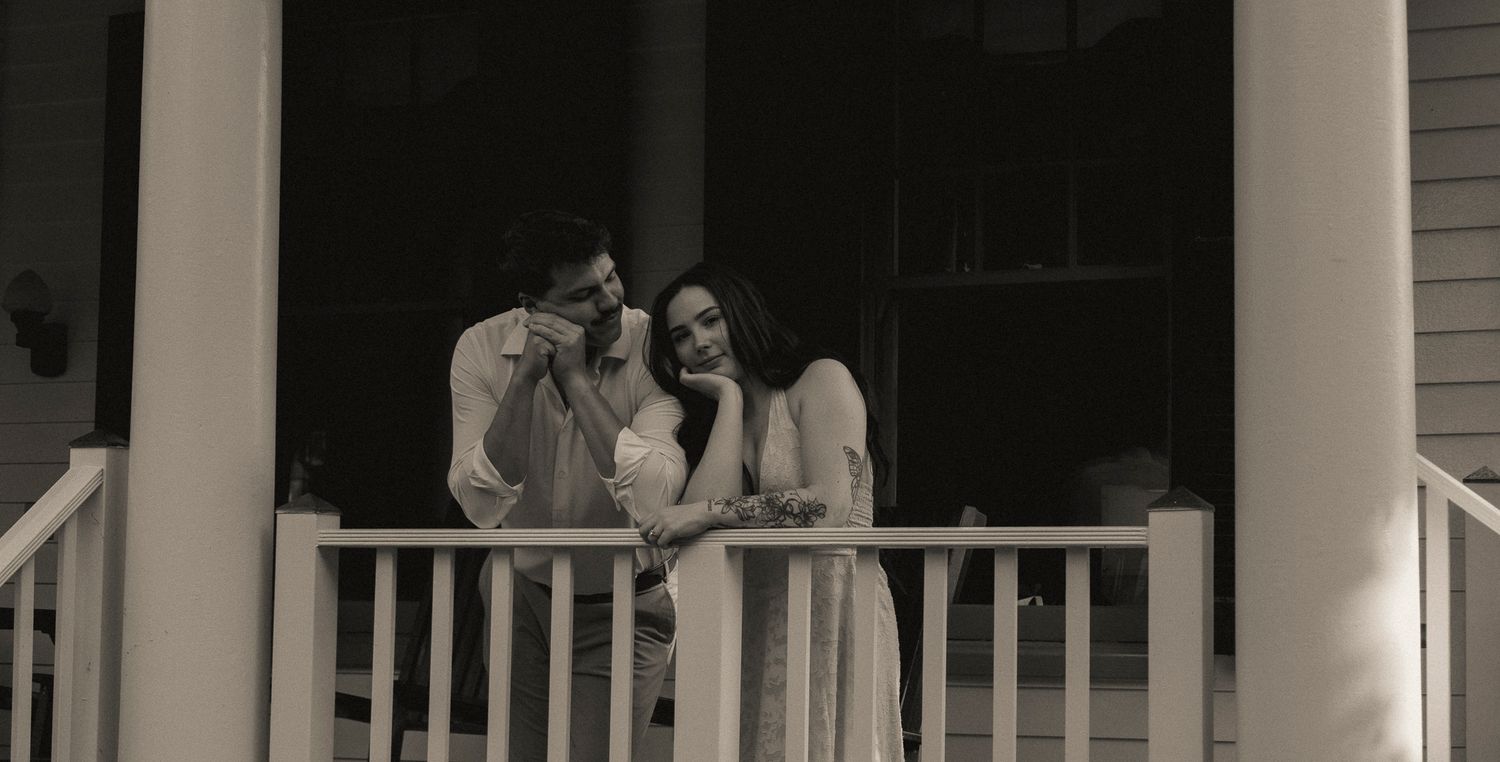 Couple sharing a romantic moment on a white porch railing in black and white photo.