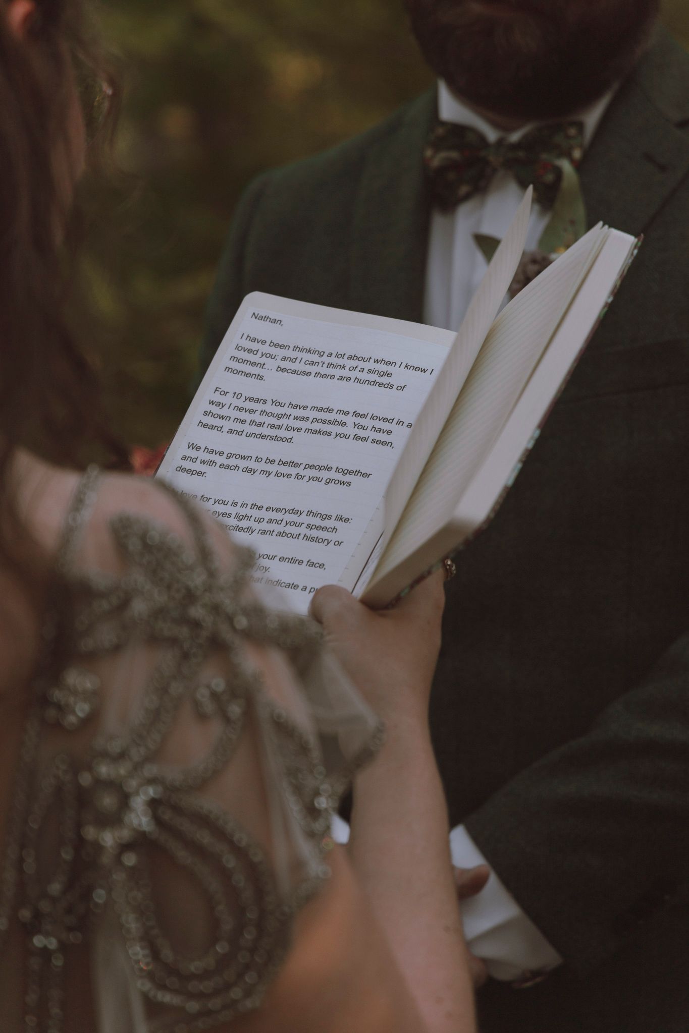 Person holding and reading from a small white book or card against a dark blurred background.