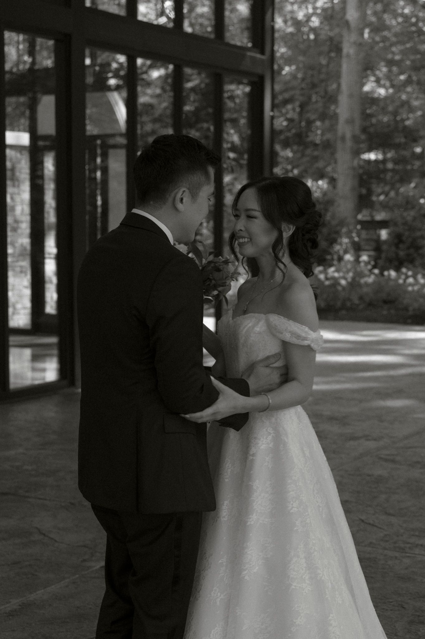 A romantic black and white wedding photo of a couple sharing an intimate moment on a sunlit porch.