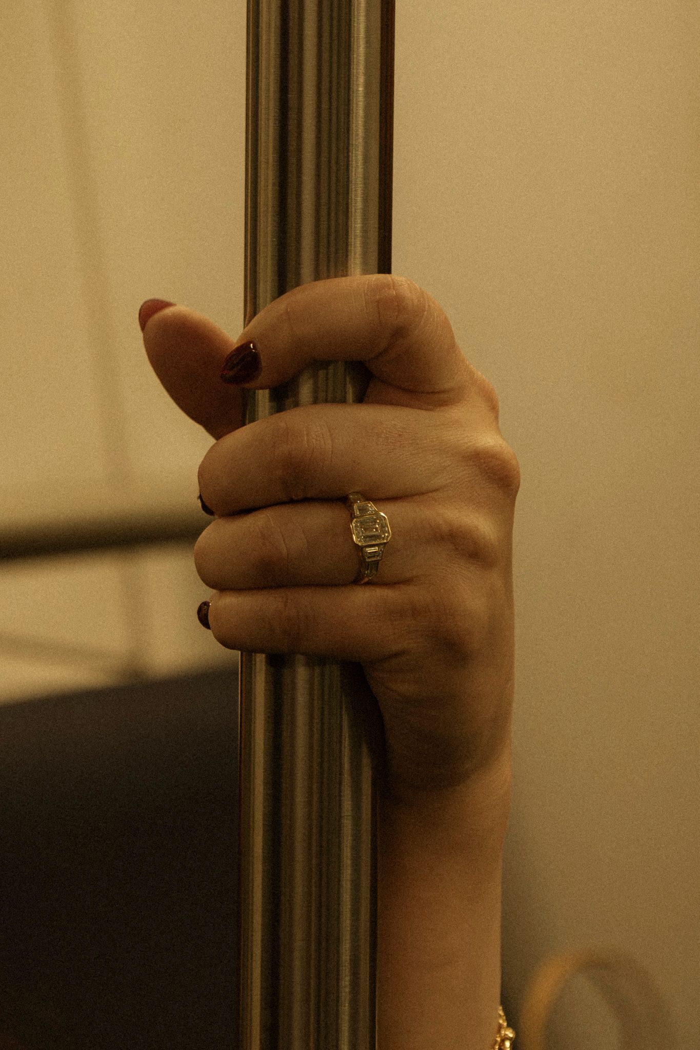 A hand wearing a ring grips a metal pole or bar in warm lighting.