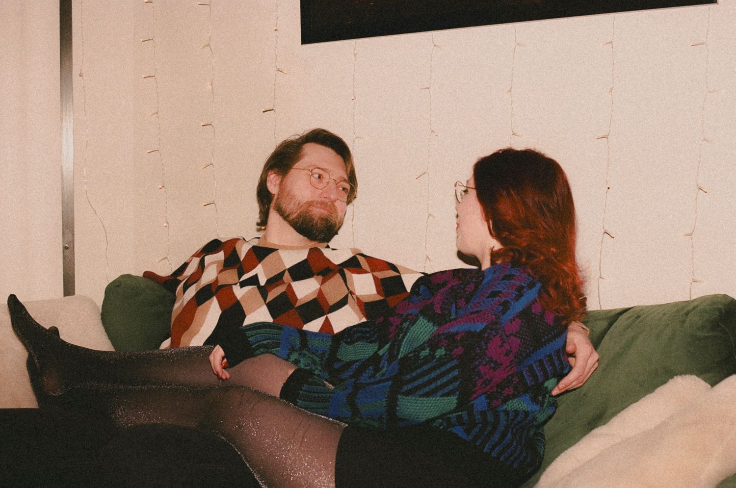 People seated in a row on a couch in a dimly lit room during a gathering.