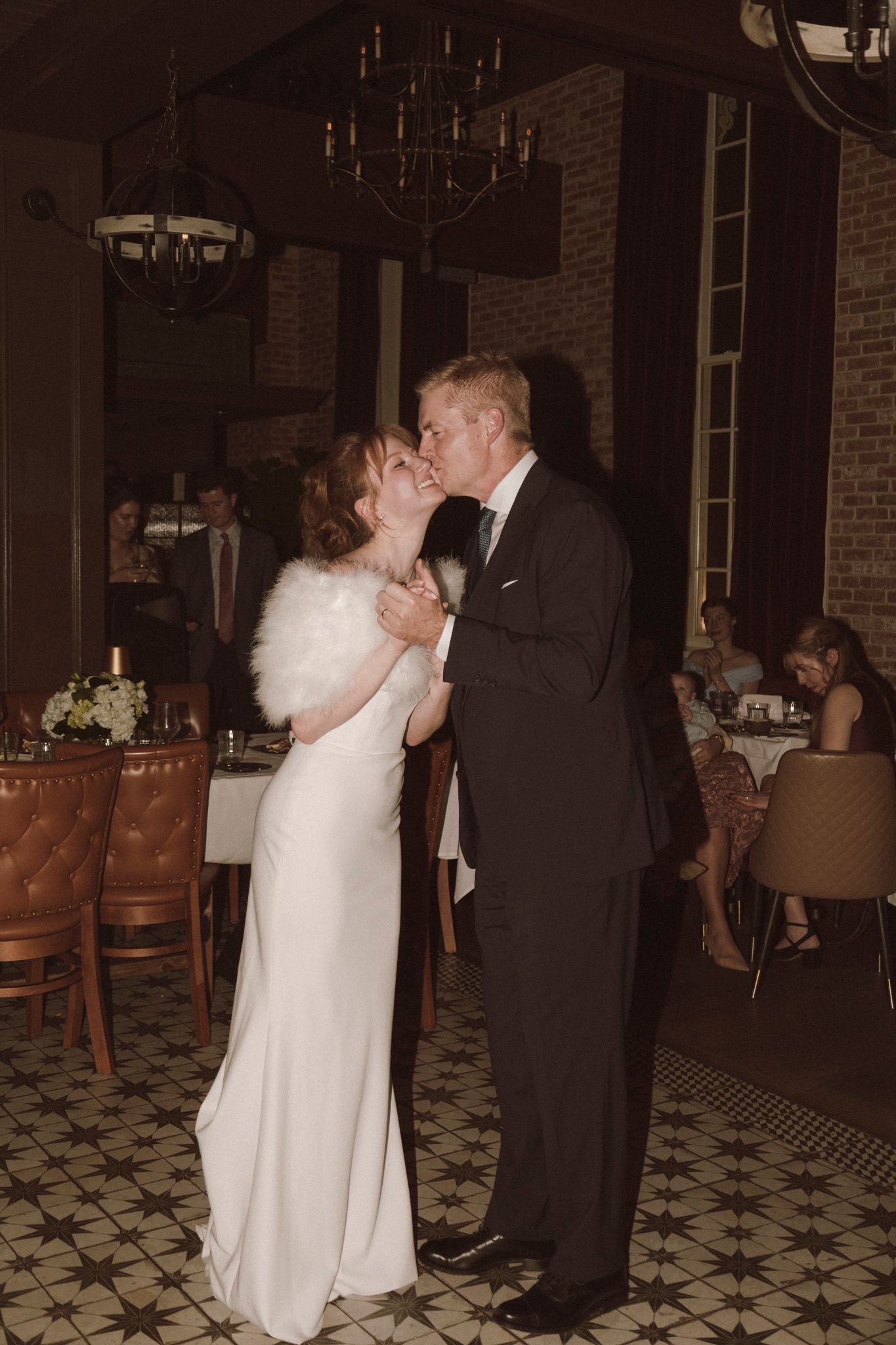Bride and groom sharing a kiss during first dance at romantic candlelit wedding reception.