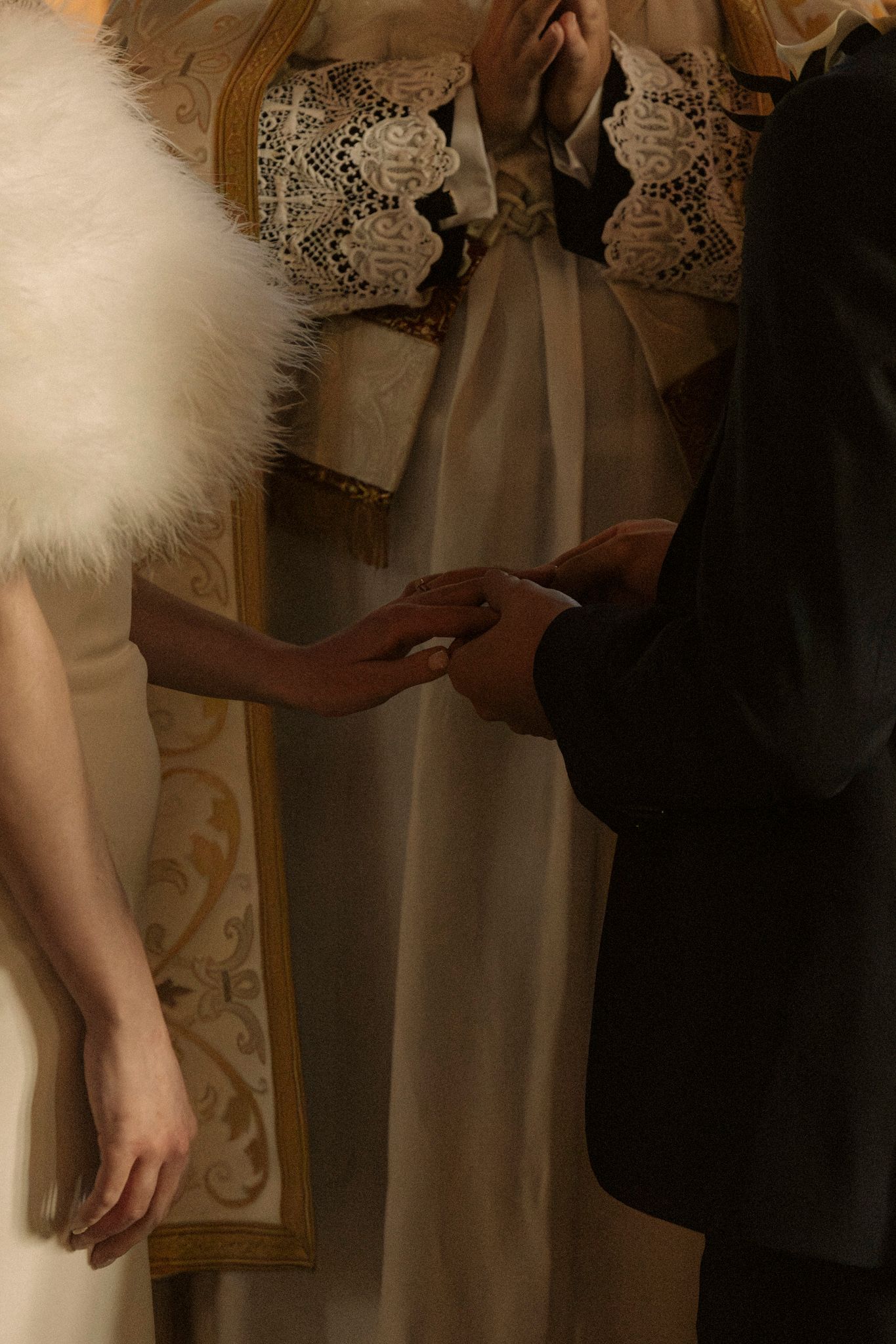 Close-up of bride and groom holding hands during wedding ring exchange ceremony at church altar.