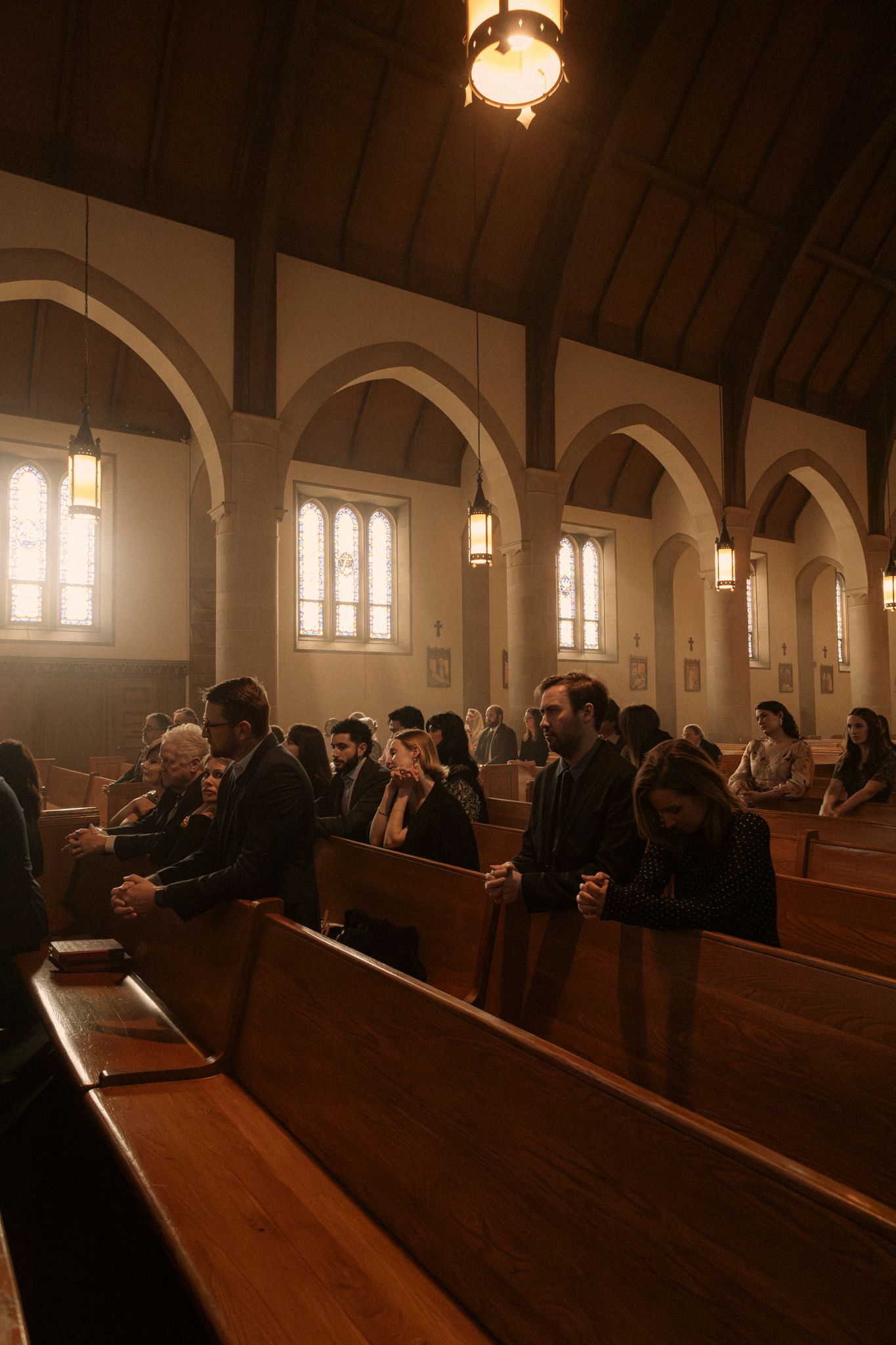 Wedding guests seated in wooden pews of beautiful arched Catholic church during ceremony.