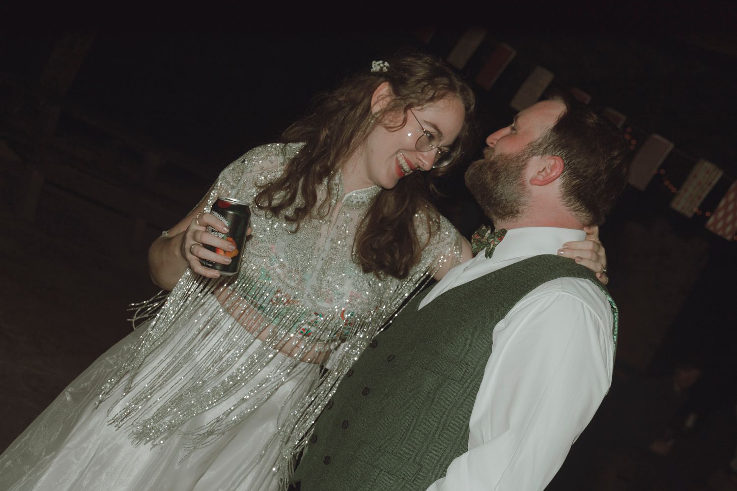 A couple in wedding attire dances together in a dimly lit room during their reception celebration.