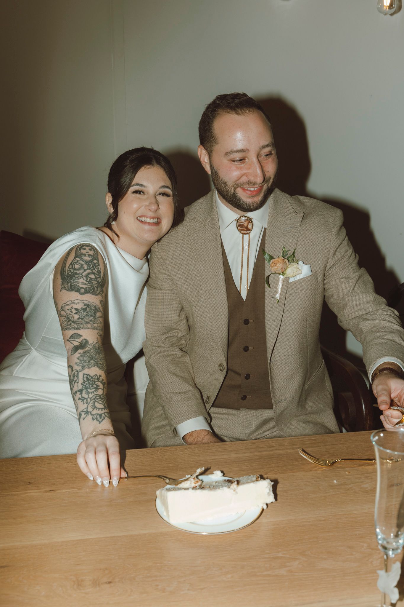 A newlywed couple sits at a wooden table during their wedding reception, sharing an intimate moment.