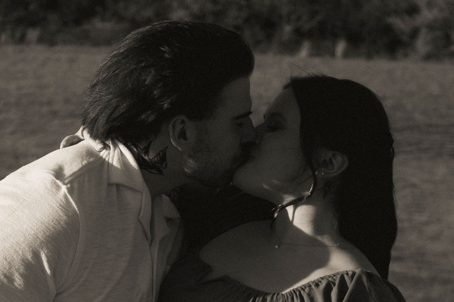 Black and white photo of a couple sharing a tender kiss outdoors.