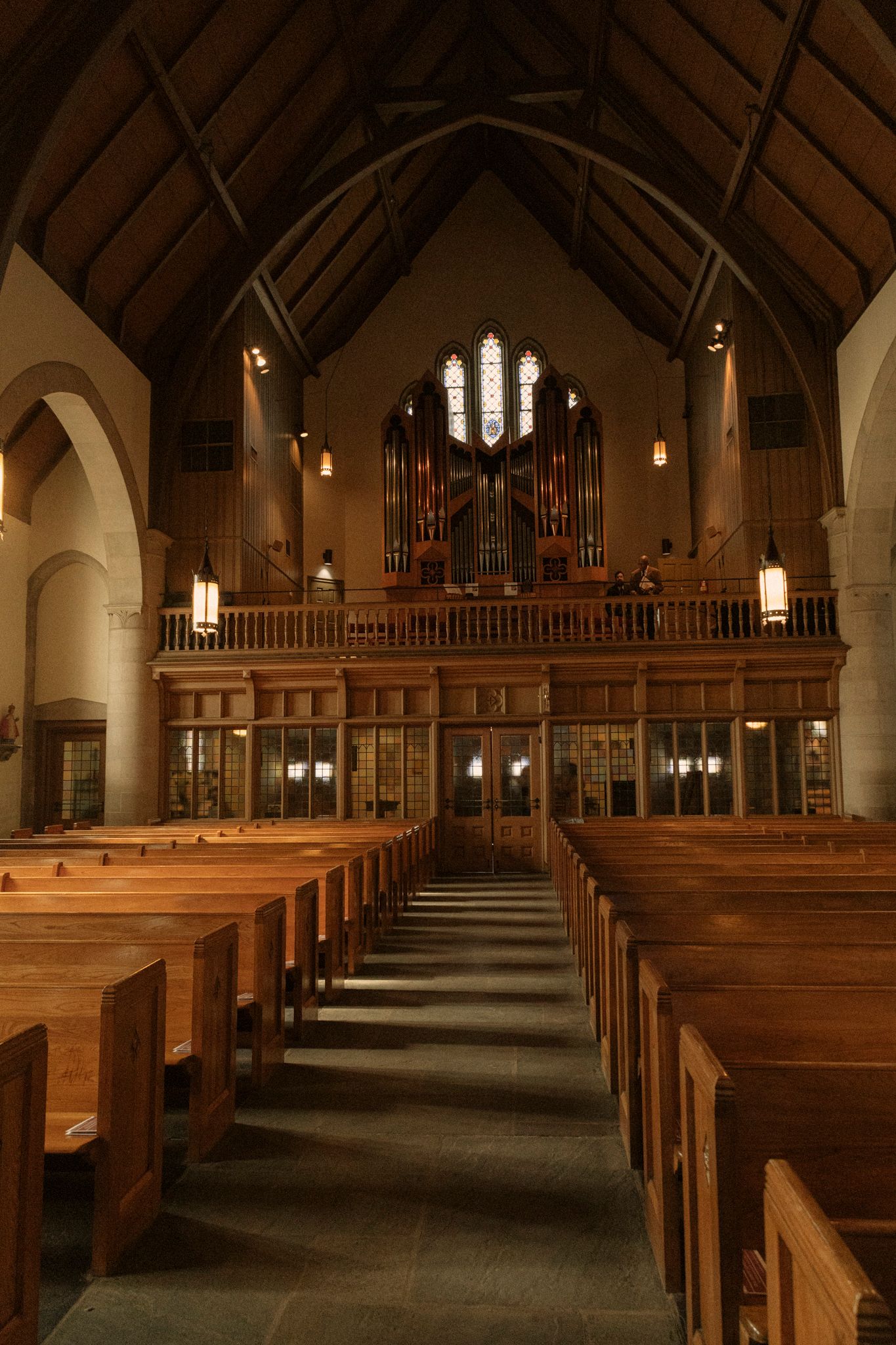 Church interior with rows of wooden pews leading to a pipe organ loft beneath a vaulted wooden ceiling.