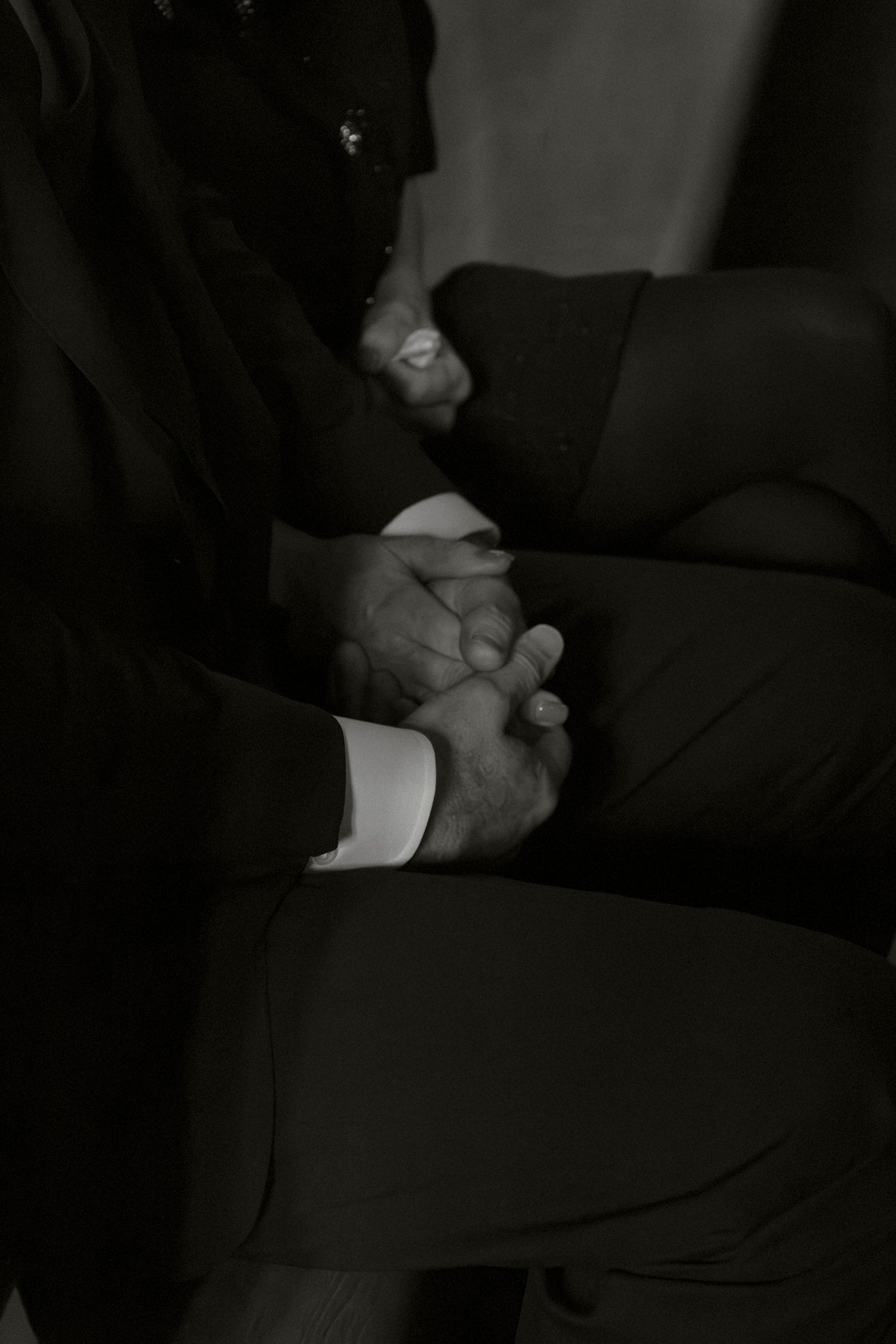 Black and white close-up of two men in suits holding hands during wedding ceremony.