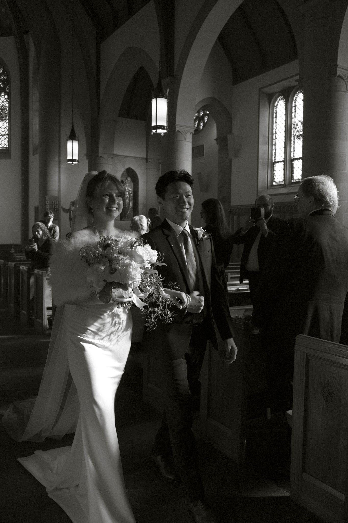 Smiling bride and groom walking down church aisle after wedding ceremony, bride holding bouquet.