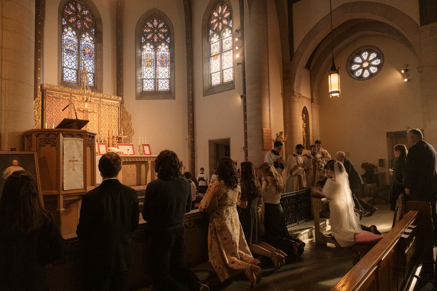 Guests stand in a candlelit church during a wedding ceremony with a bride in white gown.