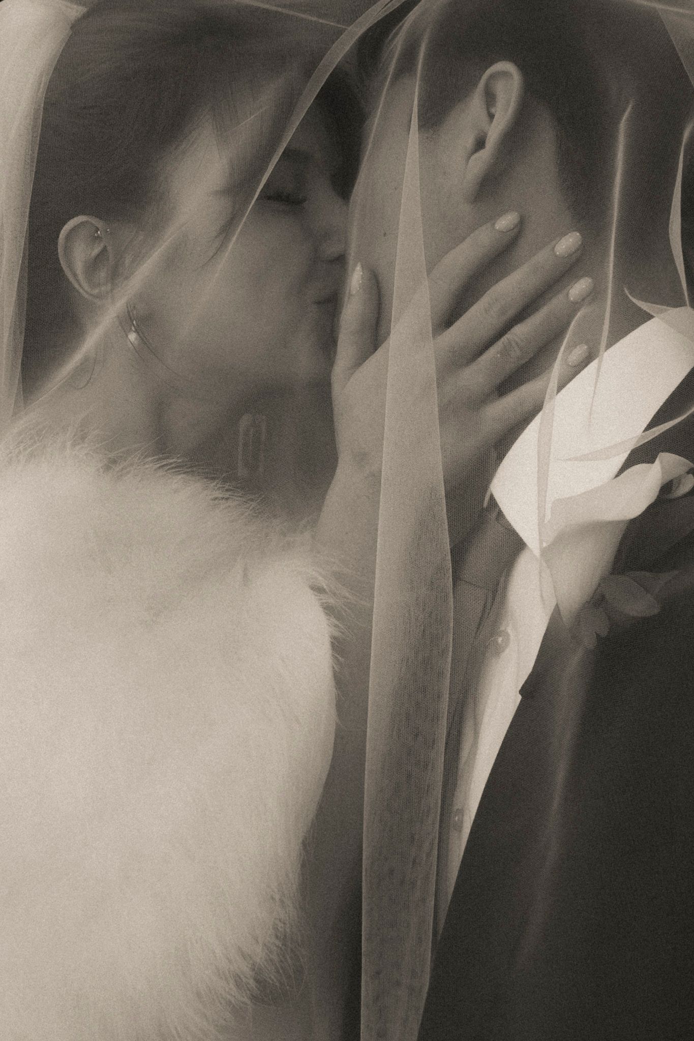 Black and white photo of bride and groom kissing under a flowing wedding veil.