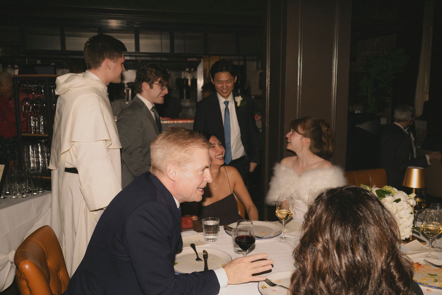 Wedding reception guests socializing at a dinner table in an elegant restaurant setting.