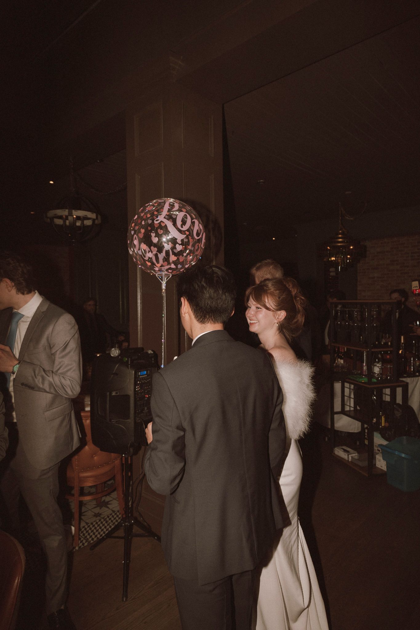 Bride in white gown with feather wrap dances with groom near a decorative balloon at wedding reception.