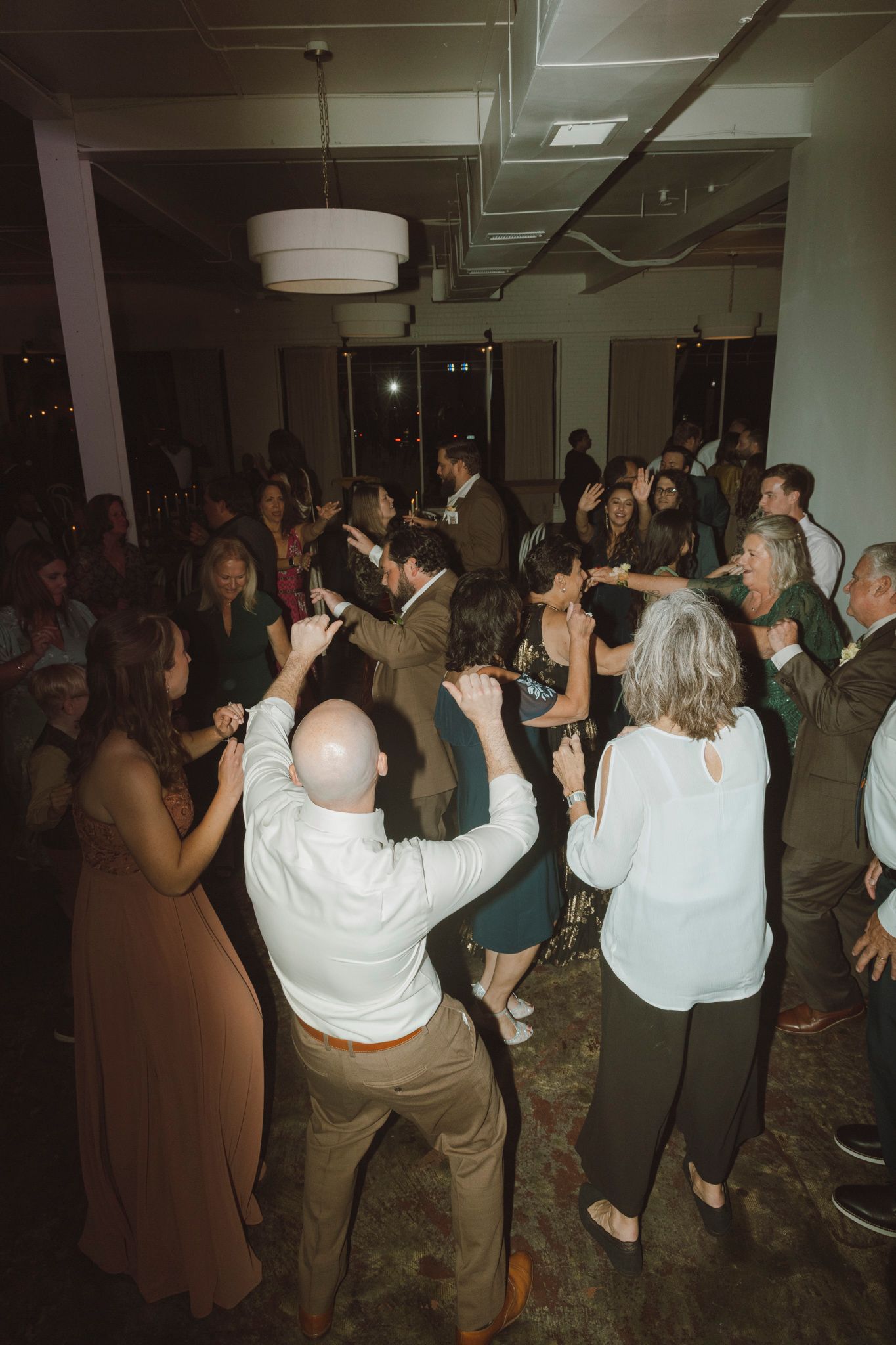 Wedding guests dance and celebrate on a dimly lit dance floor during the reception party.
