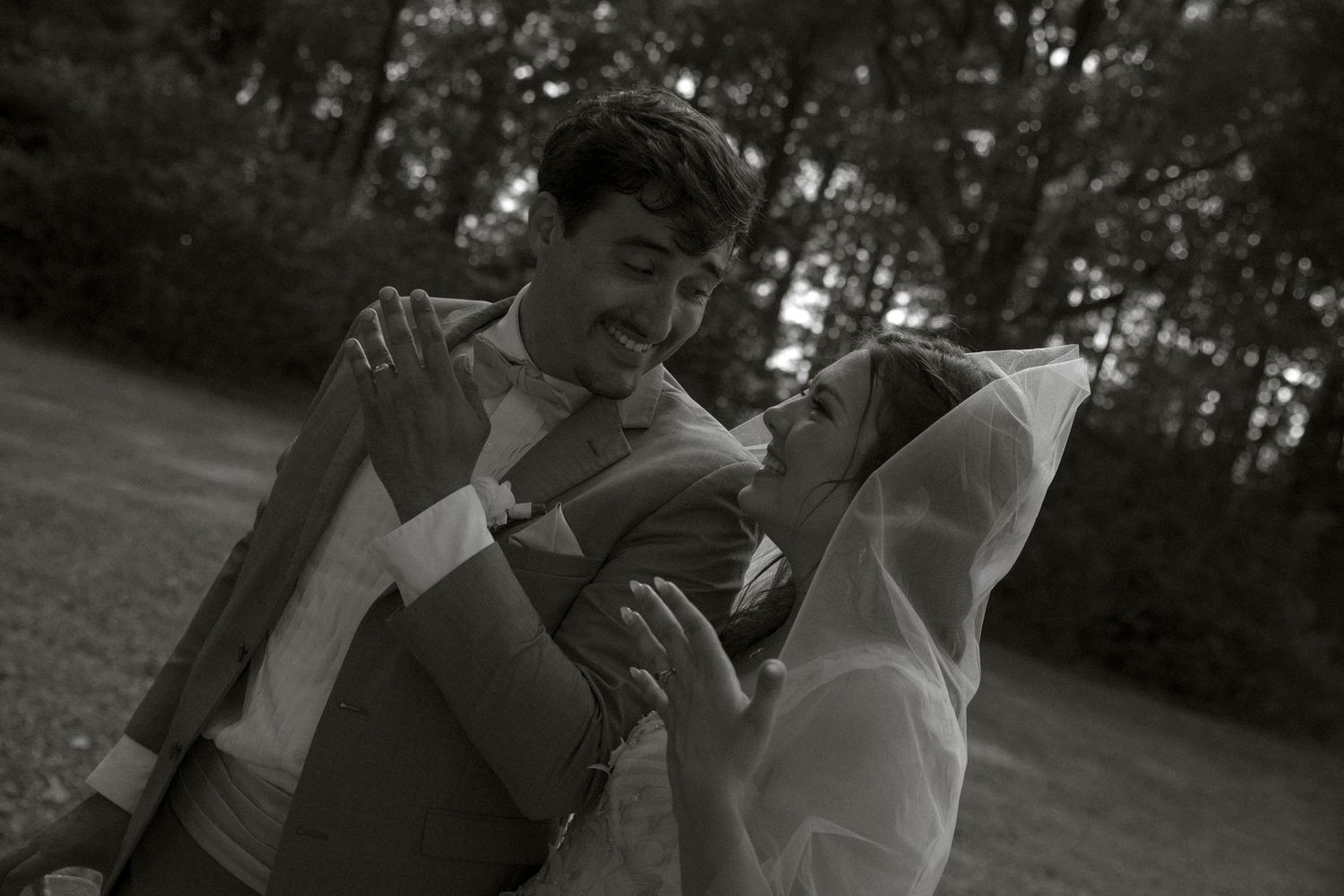 A black and white photo of a playful moment between a couple in formal attire outdoors.