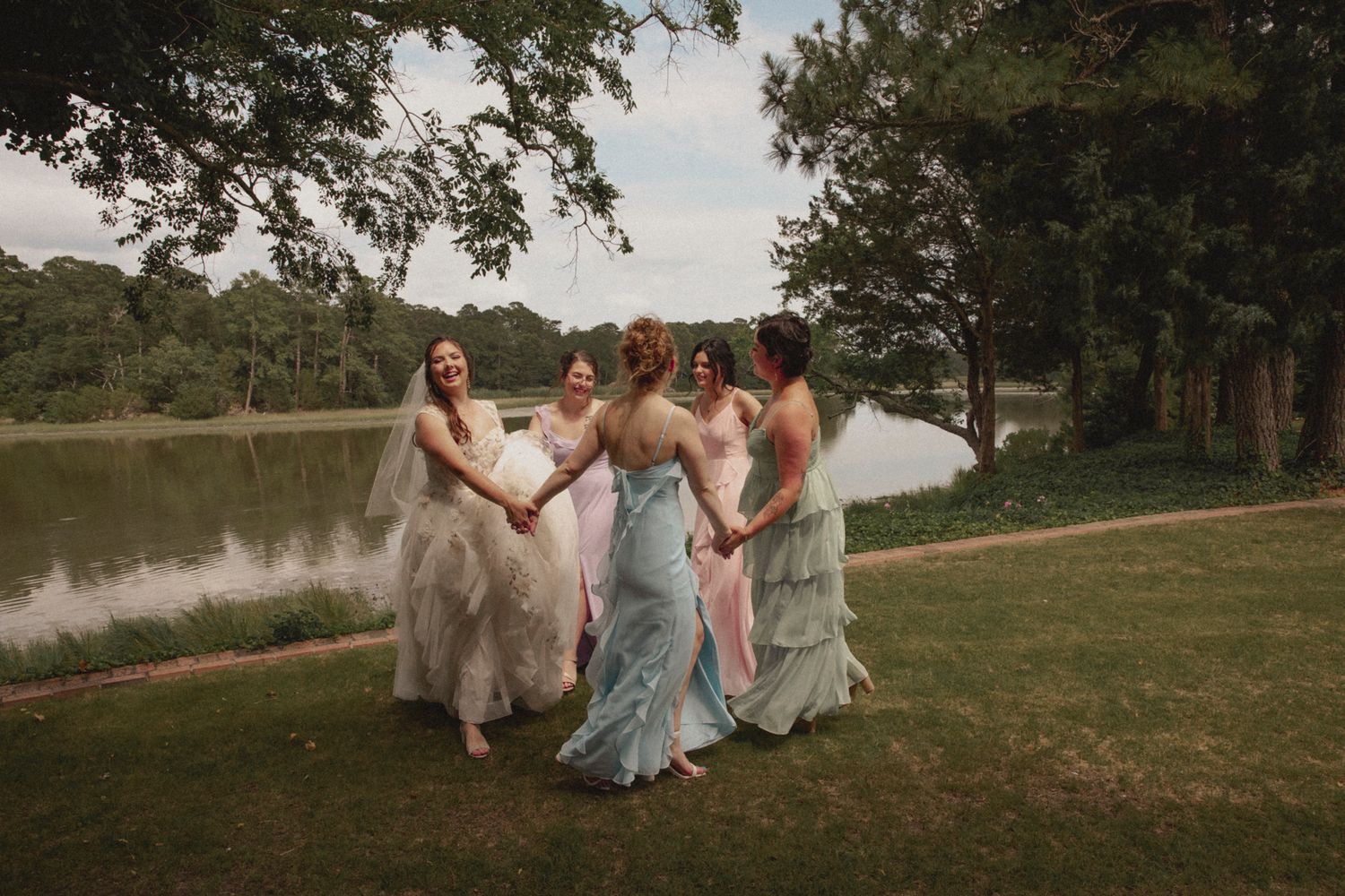 A group in formal attire runs playfully through a grassy field on a sunny afternoon.
