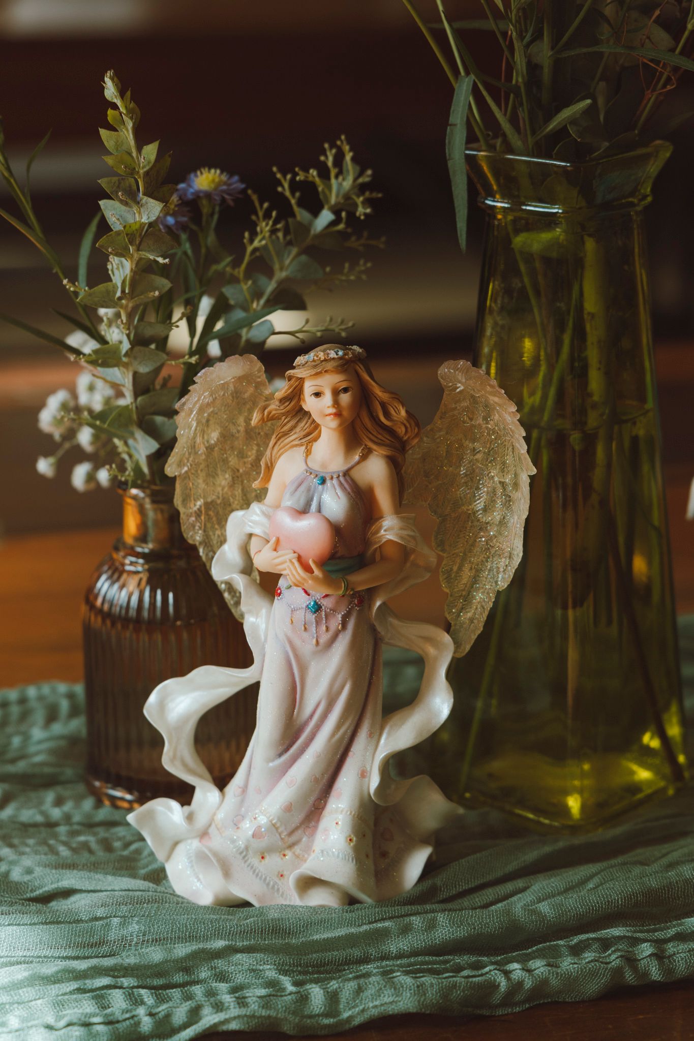 A decorative white porcelain angel figurine displayed on a turquoise cloth with glass bottles in the background.