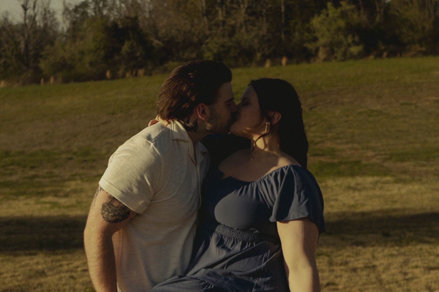 Couple sharing a romantic kiss outdoors in a sunny green field.