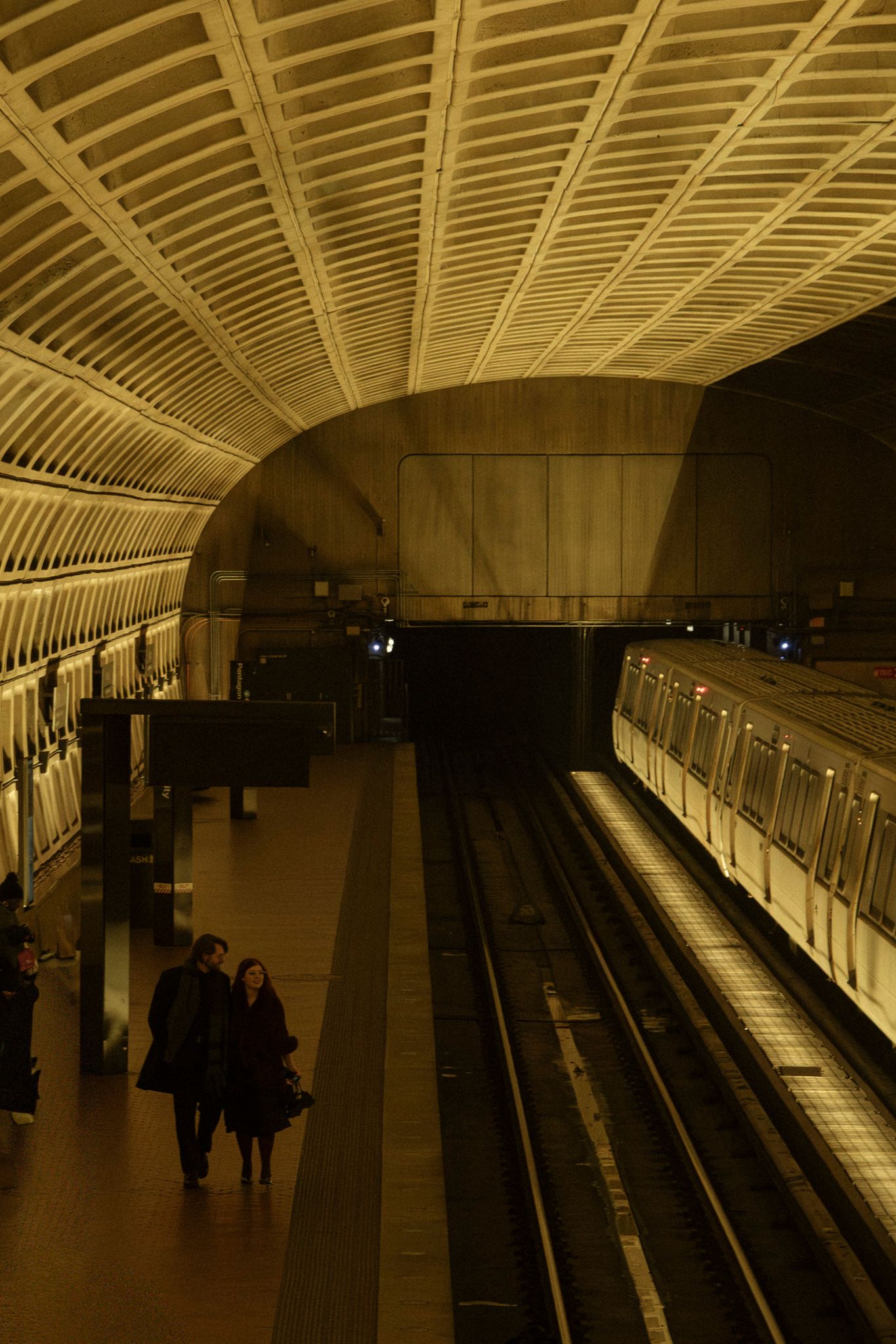 A dimly lit subway station platform with curved ceiling and fluorescent lighting stretches into the distance.