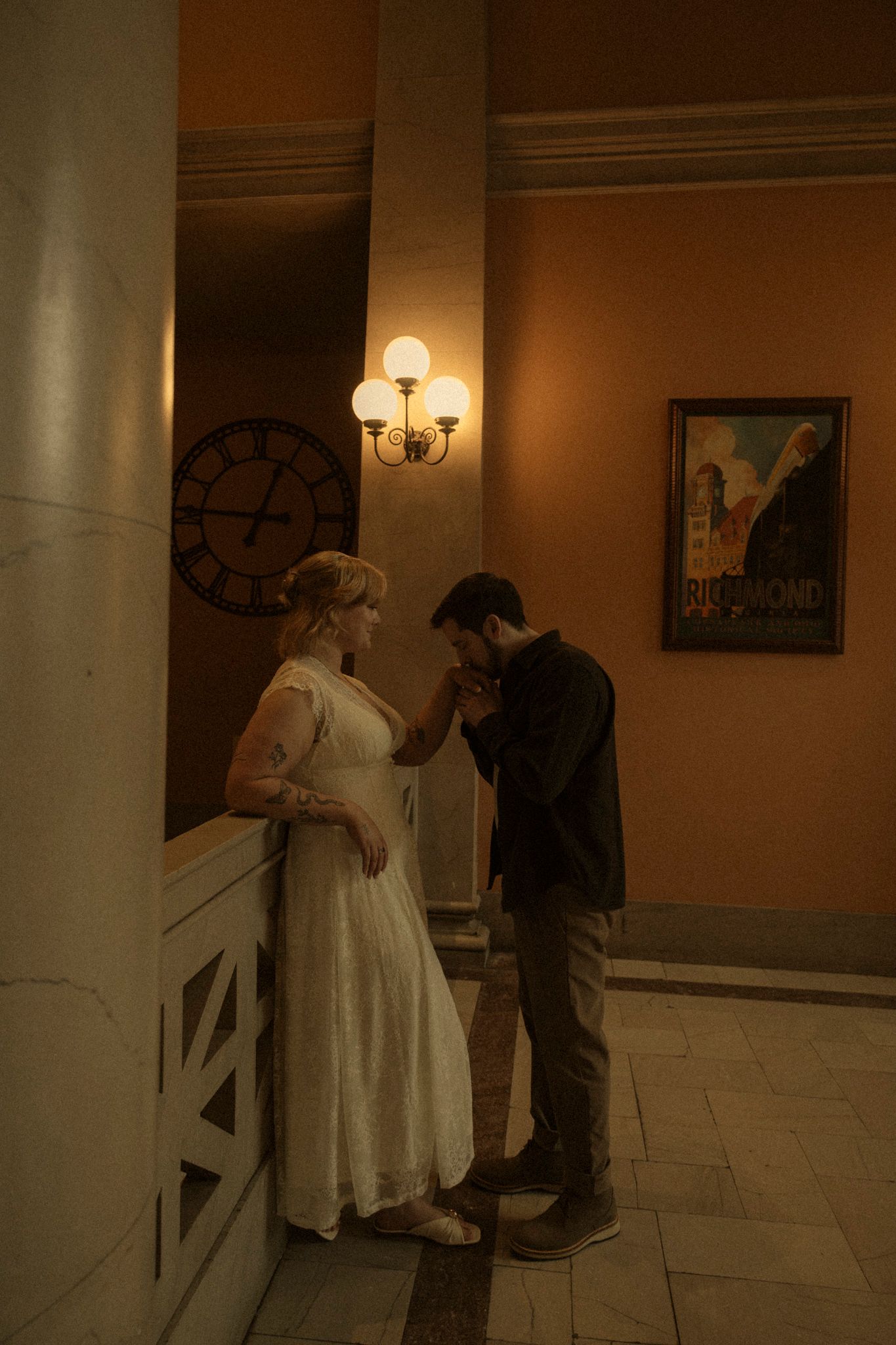 A figure in a ghostly white dress haunts a dimly lit hallway with columns and wall sconces creating an eerie atmosphere.