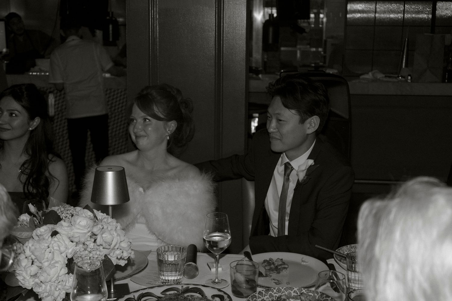 Black and white photo of bride and groom smiling together at their wedding reception dinner table.
