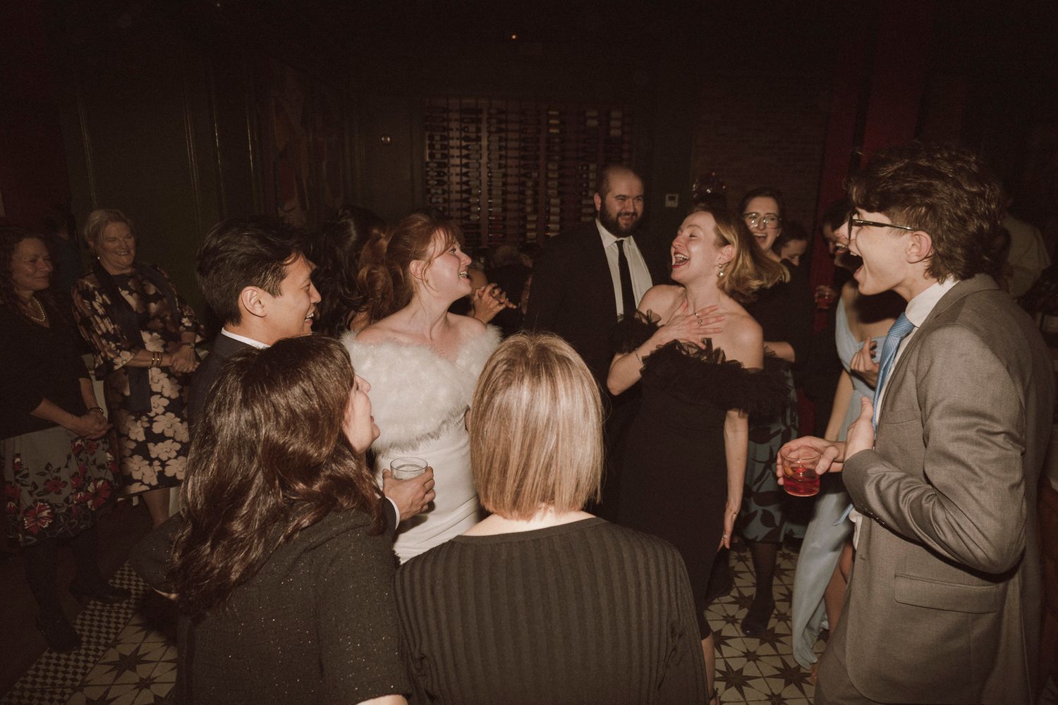 Bride in white dress celebrates joyfully with wedding guests at lively indoor reception.