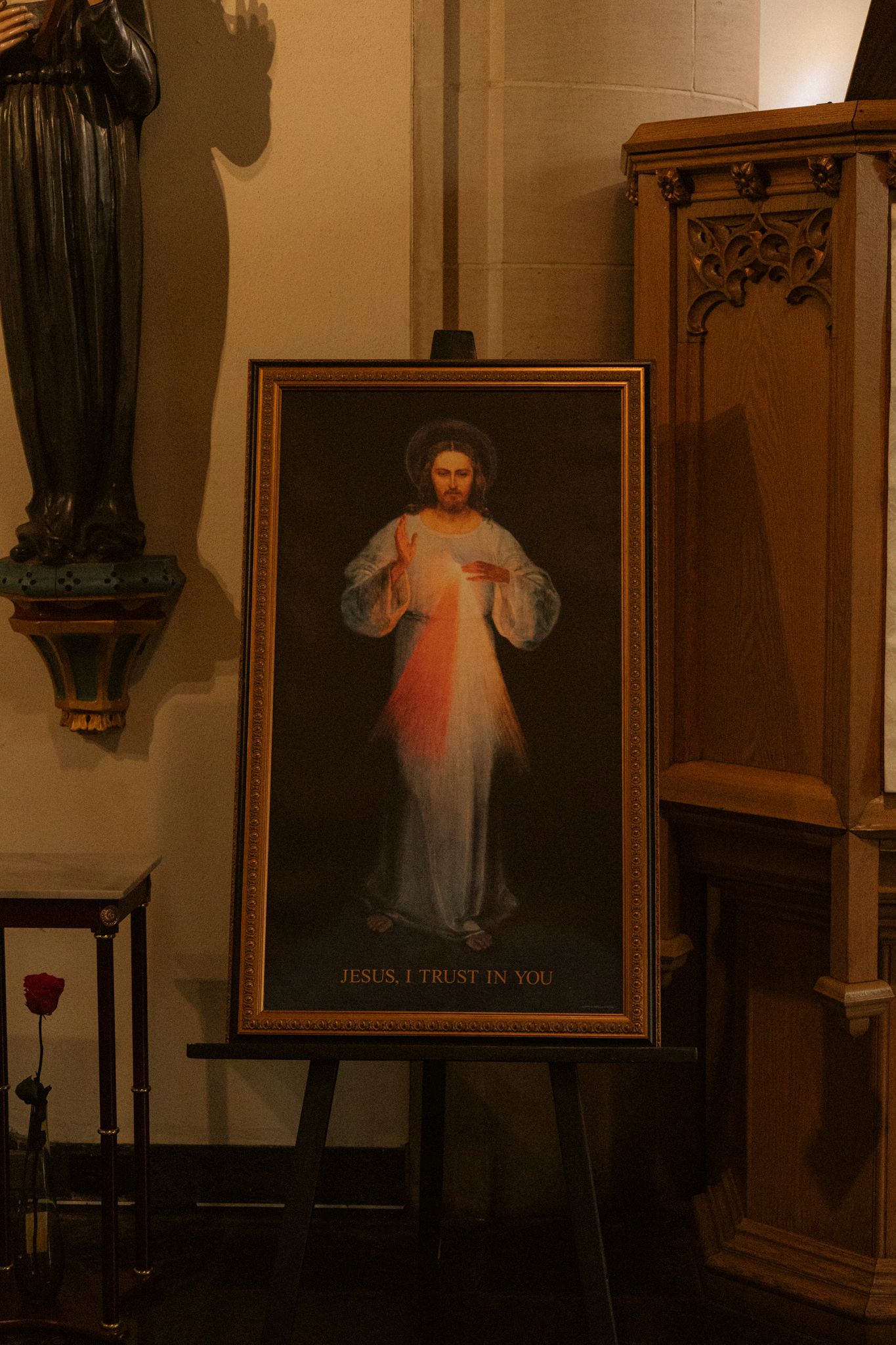 Divine Mercy painting of Jesus on easel with text Jesus I Trust In You in church interior.