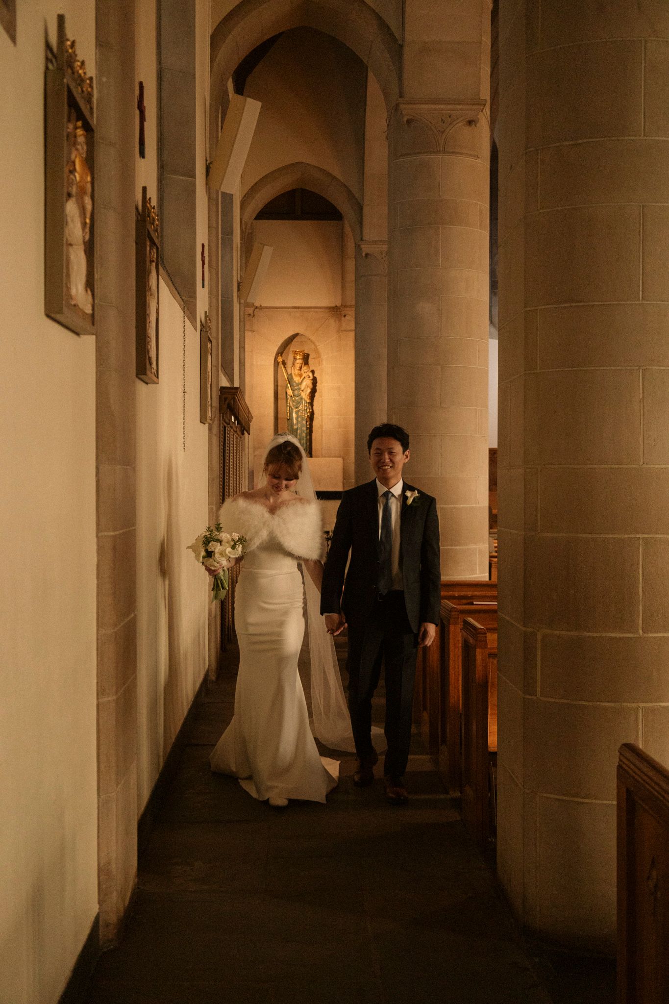 Bride and groom walking through a warmly lit stone church aisle after their wedding ceremony.