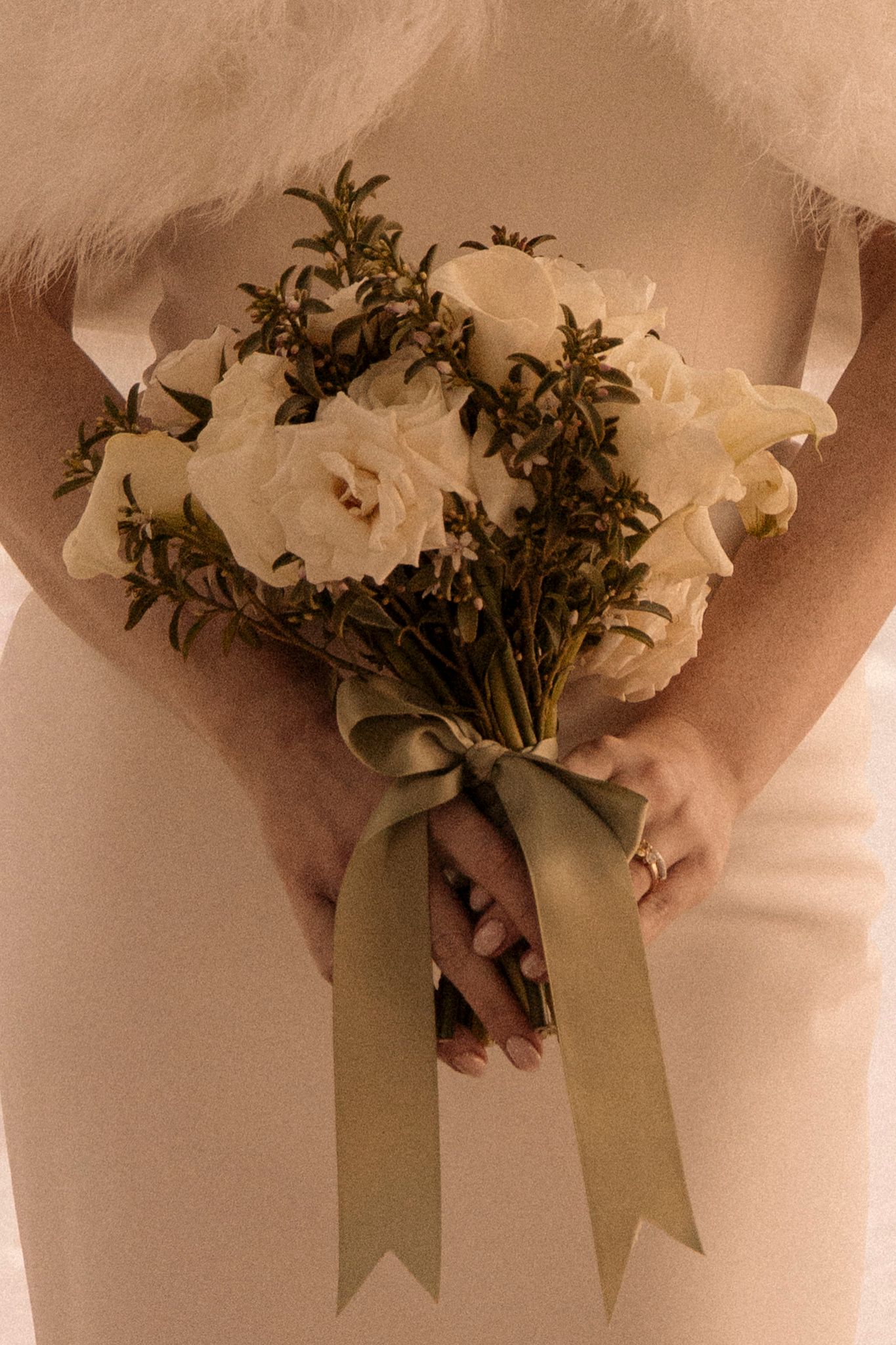 Bride holds an elegant bouquet of white roses tied with a sage green ribbon bow at her wedding.
