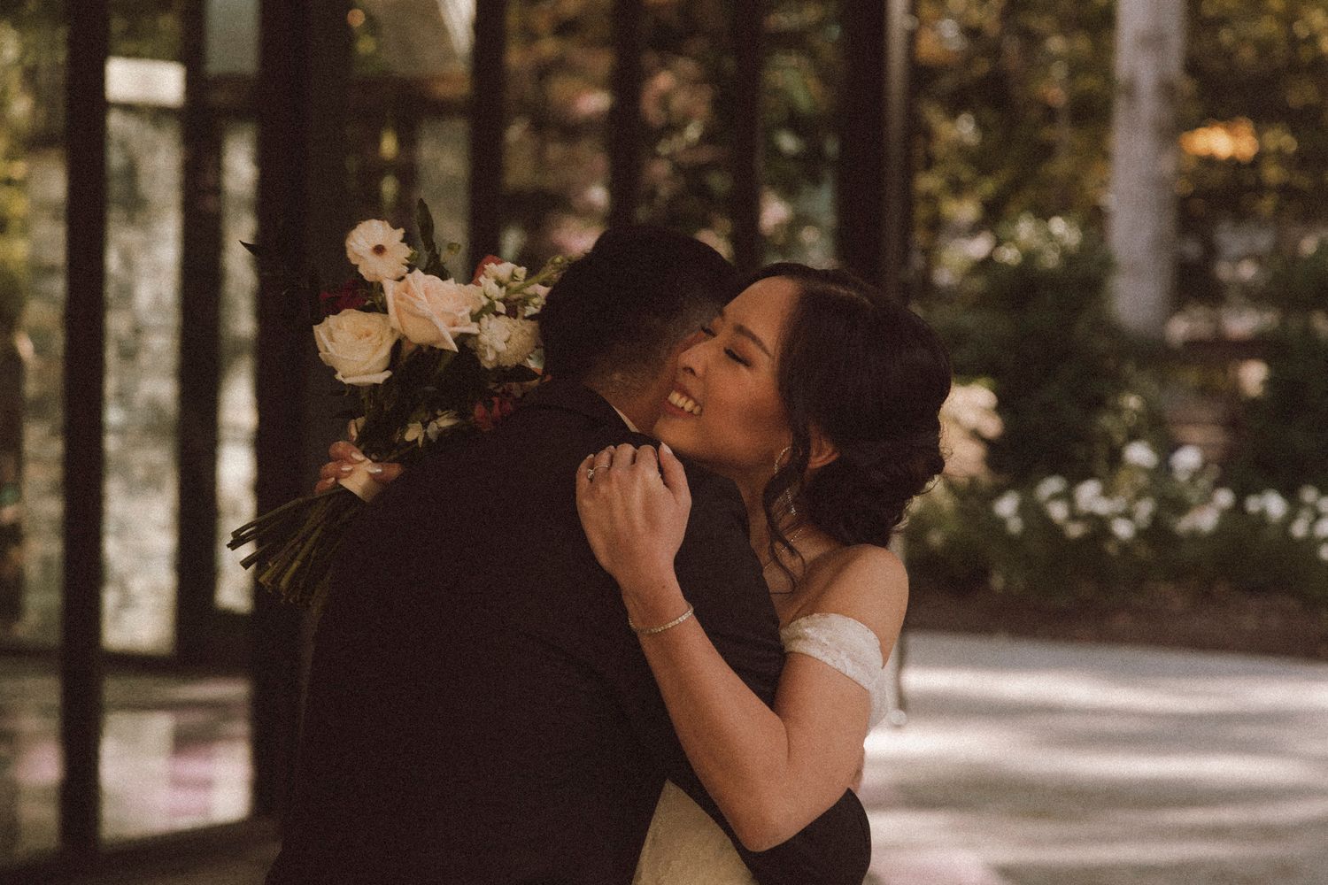 A couple in formal attire shares a romantic dance together in a sunlit outdoor garden setting.