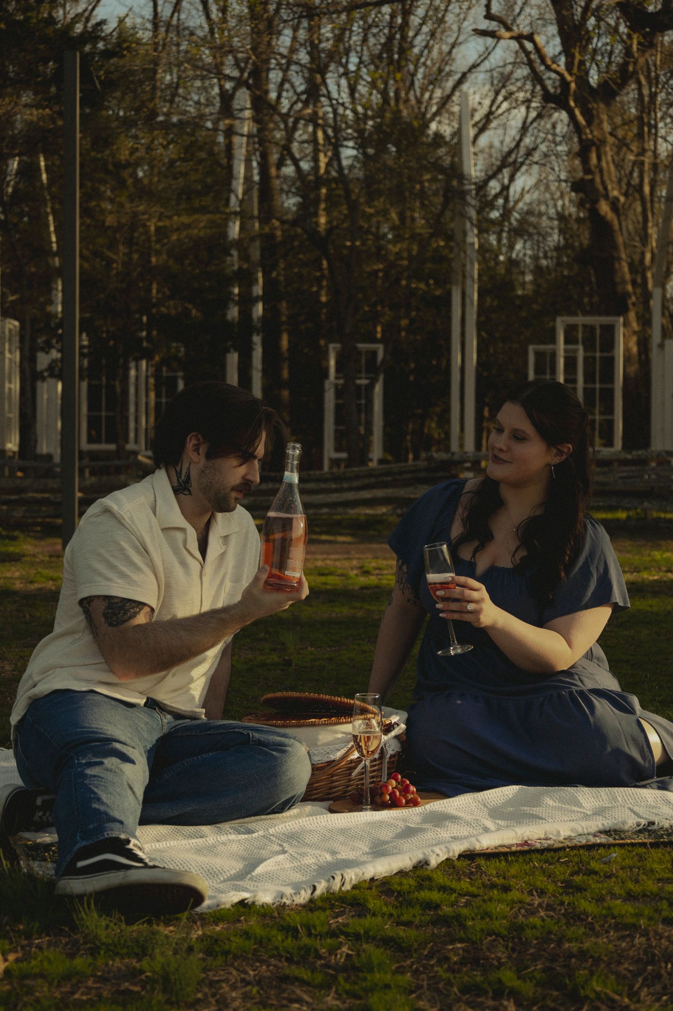 Couple enjoying a romantic outdoor picnic on a blanket, sharing wine and snacks in a sunny park setting.