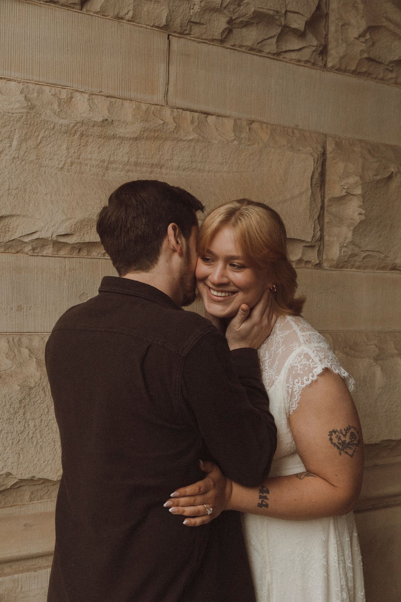 Intimate moment captured against textured limestone wall in warm sepia tones.