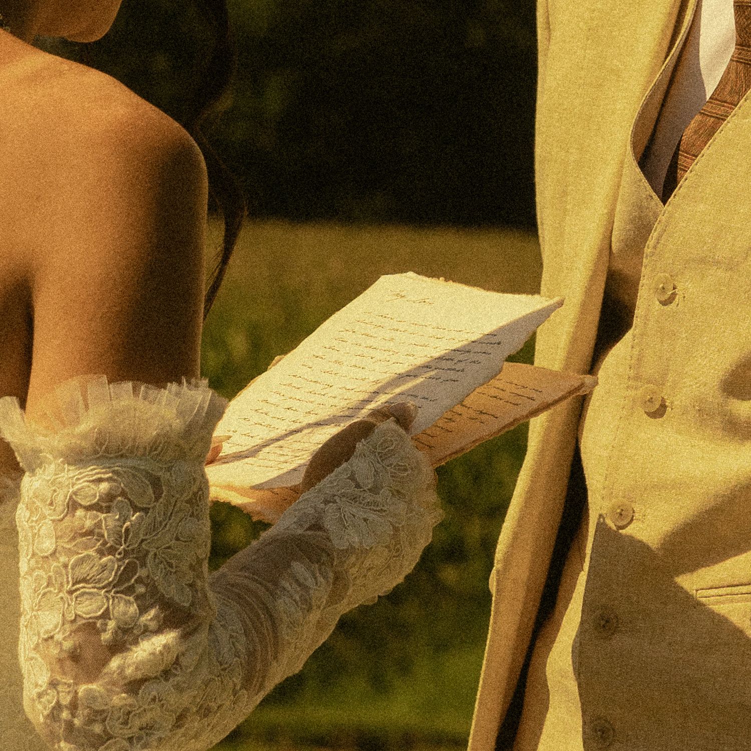 Bride in lace gloves reading handwritten wedding vows to groom outdoors in golden light.