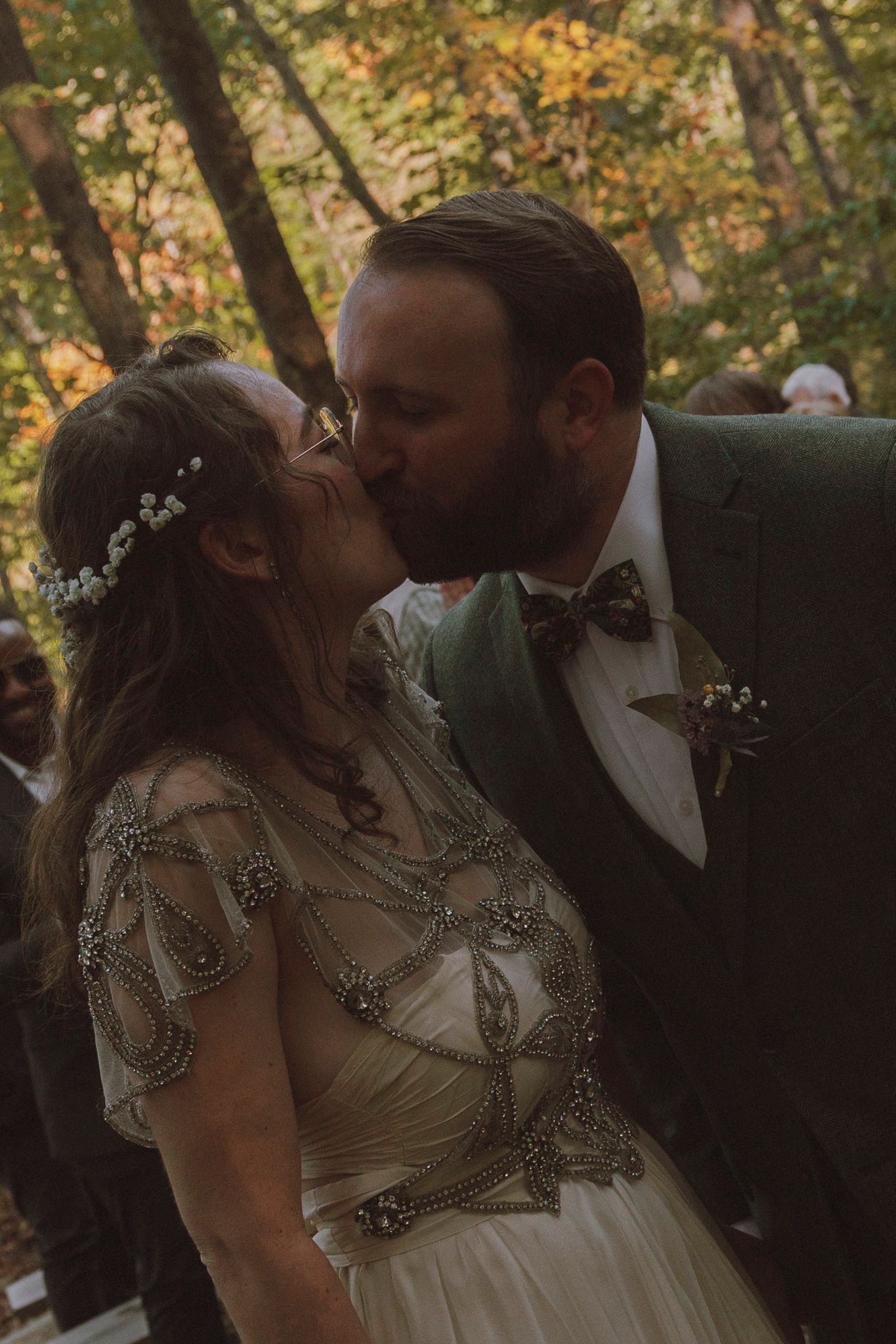 A romantic kiss sequence between newlyweds at an outdoor autumn wedding ceremony with fall foliage in the background.